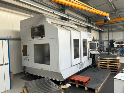 Spinner VC 1650 CNC gép, elölnézetben, vezérlőpanellel, nagy ablakokkal és a közelben raklapokkal egy műhelyben.