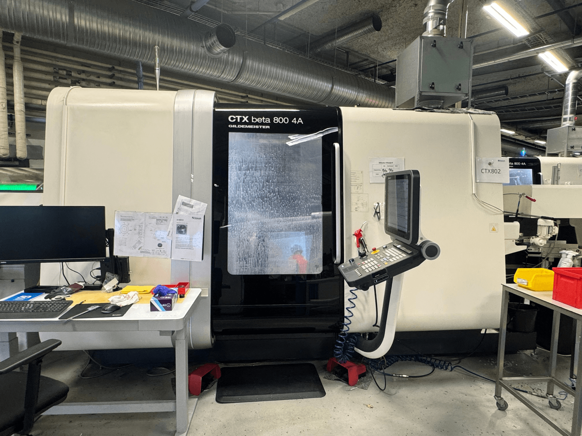 CTX beta 800 4A CNC-gép egy műhelyben, oldalnézetben a vezérlőpanel és a szerszámokkal és dokumentumokkal zsúfolt munkaterület.