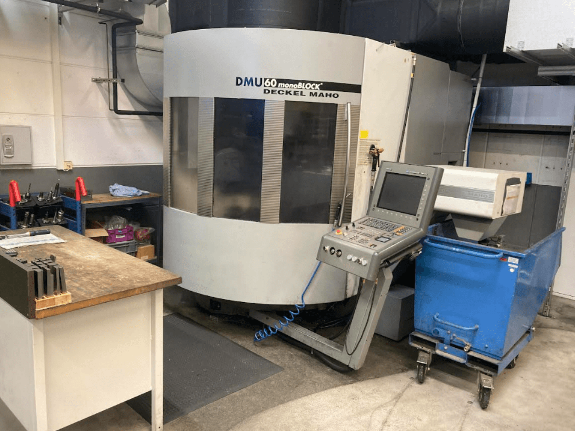 DMG MORI DMU 60 Monoblock függőleges megmunkálóközpont, előlnézet a vezérlőpanellel, a munkaterülettel és a kék szerszámkocsival.