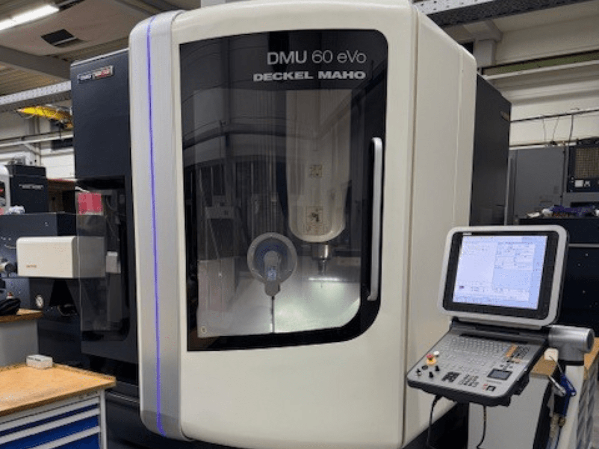 DMU 60 eVo by DECKEL MAHO, CNC marógép előlapja vezérlőpanellel és kijelzővel, precíziós alkatrészek bemutatásával.