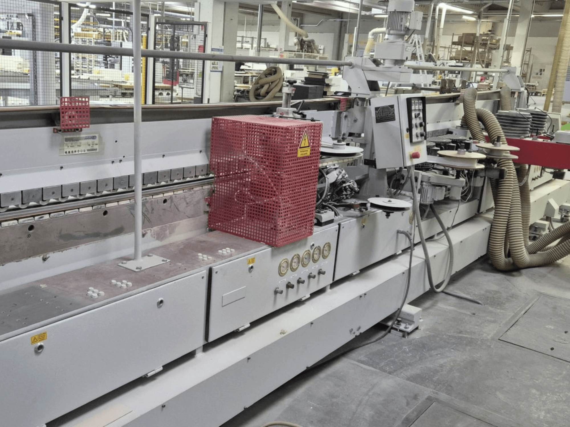 Élszalagozó gép vezérlőpanellel, szívótömlőkkel és piros biztonsági burkolattal, oldalnézetből.