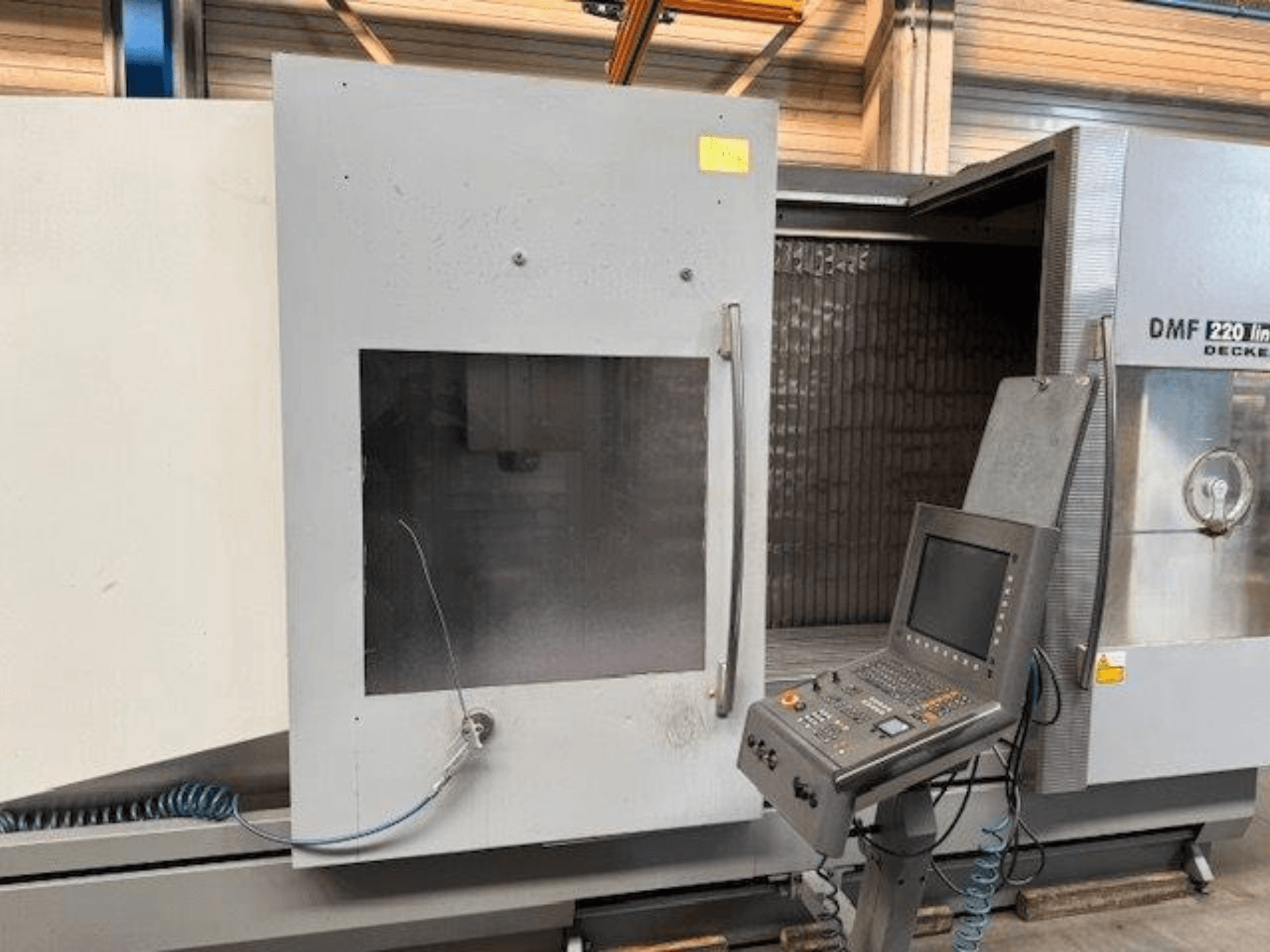 A DECKEL MAHO DMF 220 Lineáris függőleges megmunkálóközpont előlapja, a vezérlőpanel és a nyitott gépajtó bemutatásával.