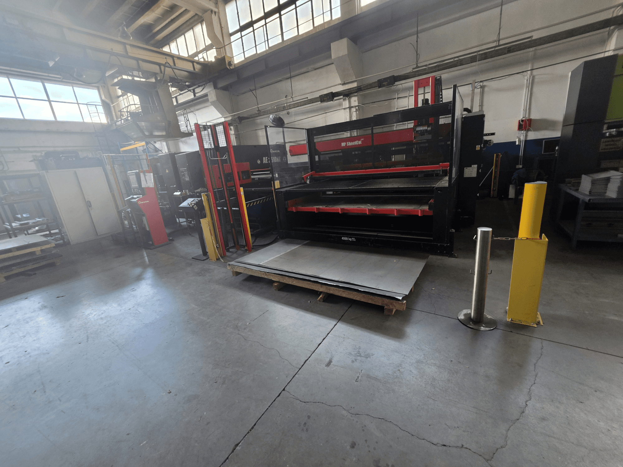 AMADA AE-2510NT CNC lyukasztógép a raktárban, oldalról nézve, a gép felállítása és a fémlemezek láthatók.