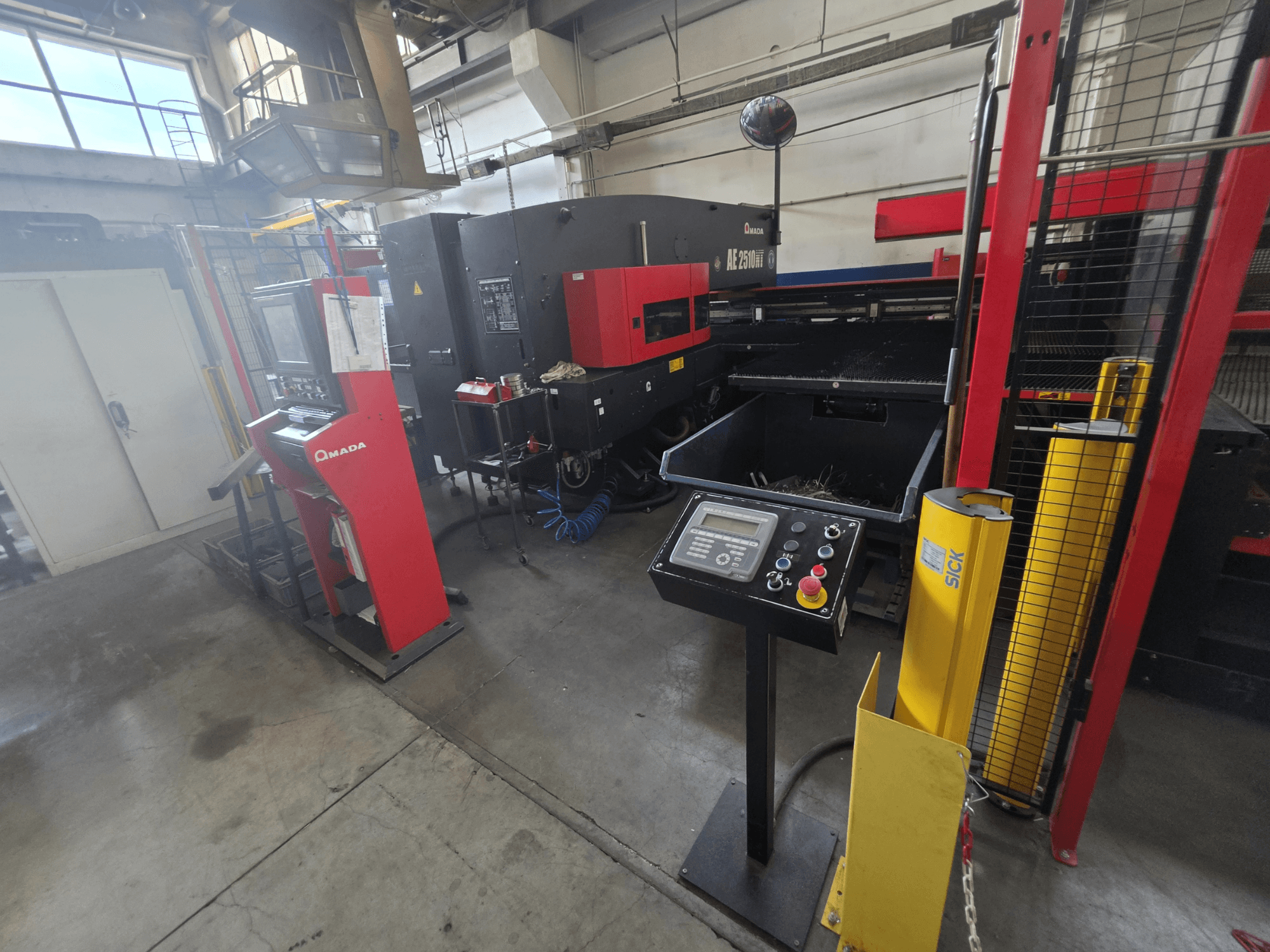 AMADA AE-2510NT CNC lyukasztógép, elölnézet a vezérlőpanellel, a biztonsági berendezésekkel és a környező ipari környezettel.