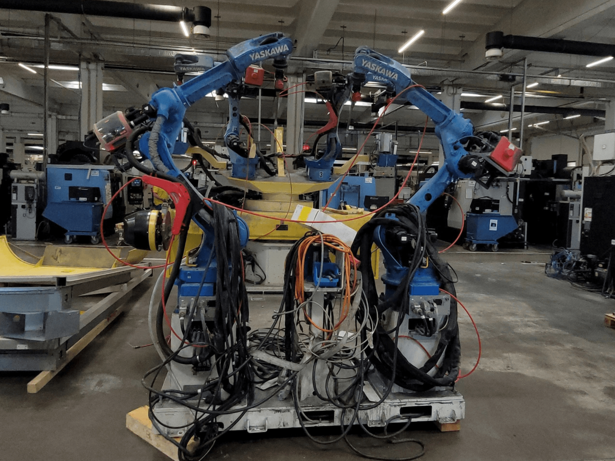 Yaskawa RWC L1_OS 15330 robothegesztő cellája, elölnézetből, két kék robotot ábrázolva, hosszú kábelekkel és hegesztőszerszámokkal.