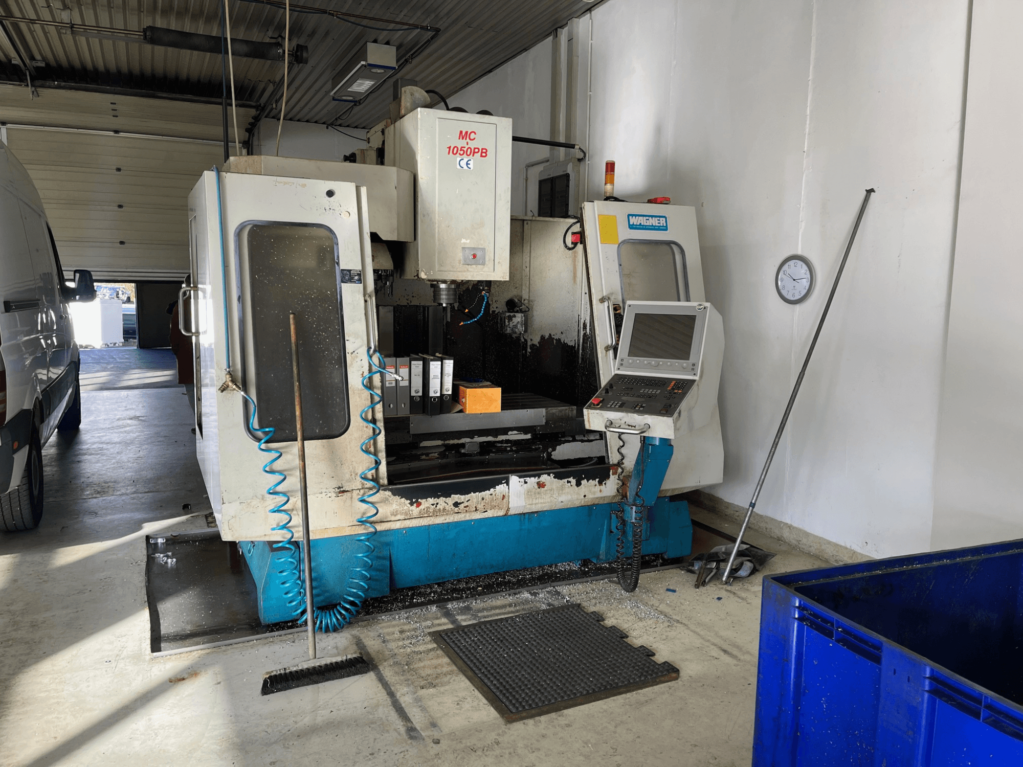 WAGNER MC 1050PB CNC-gép műhelyben, elölnézetben, vezérlőpult és munkaterület; látható a kék légtömlő és a tisztítószerszámok.
