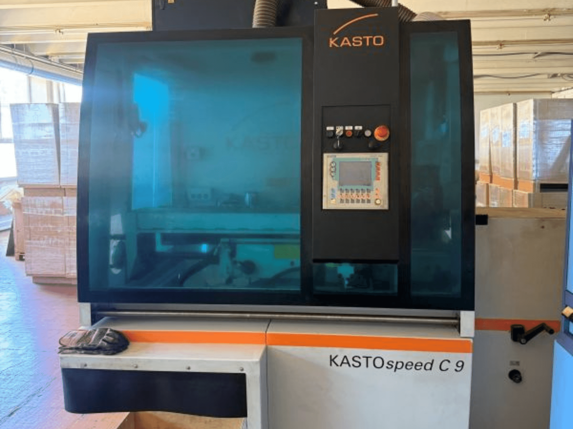 A KASTO KASTOspeed C 9 körfűrész elölnézete, a vezérlőpanellel és a biztonsági üveggel, háttérben fa rekeszekkel.