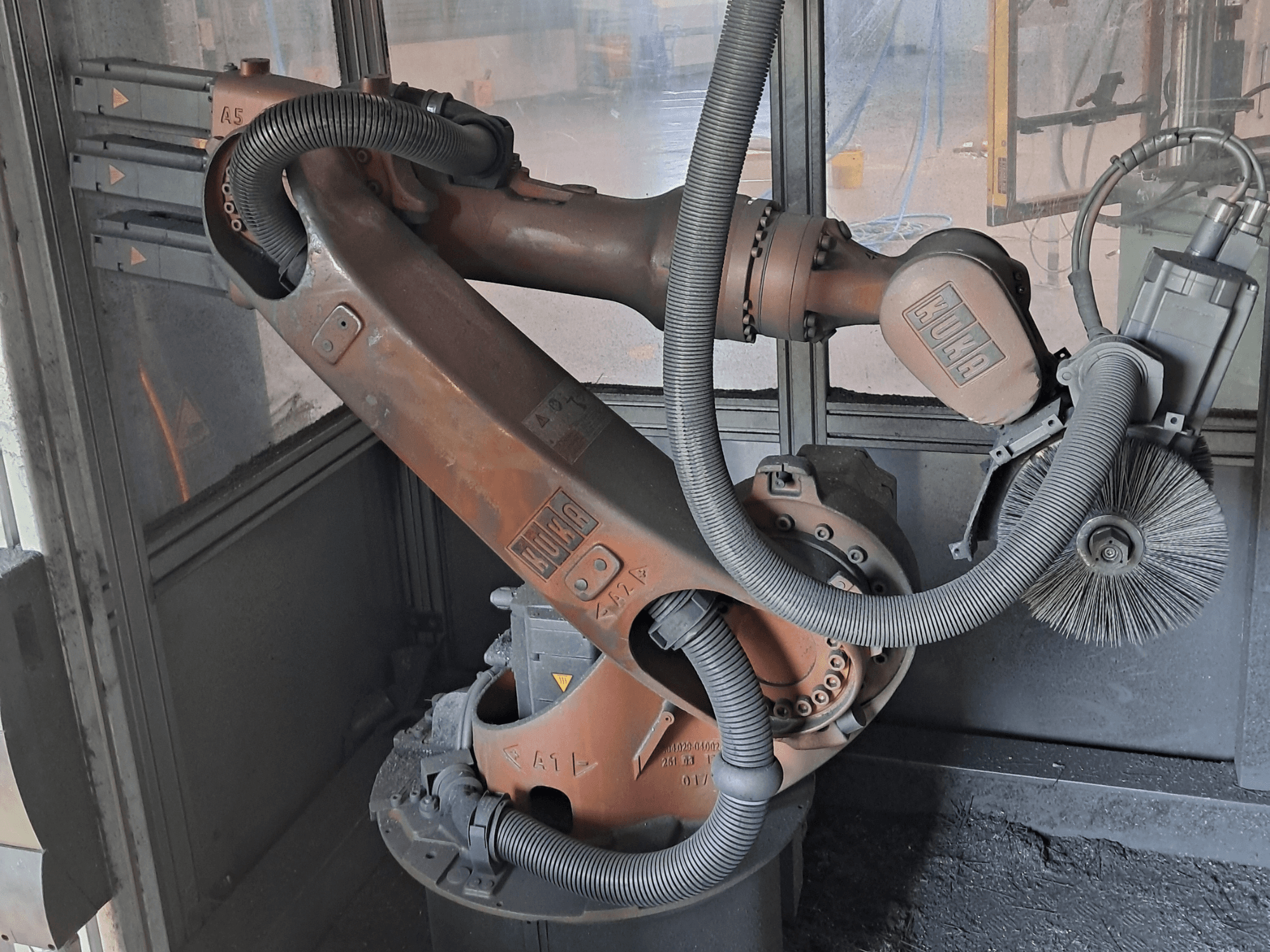 A KUKA KR 16-2 robotkar oldalnézetben, a kábelekkel, kefékkel és mechanikus csuklókkal együtt, munkakörnyezetben.