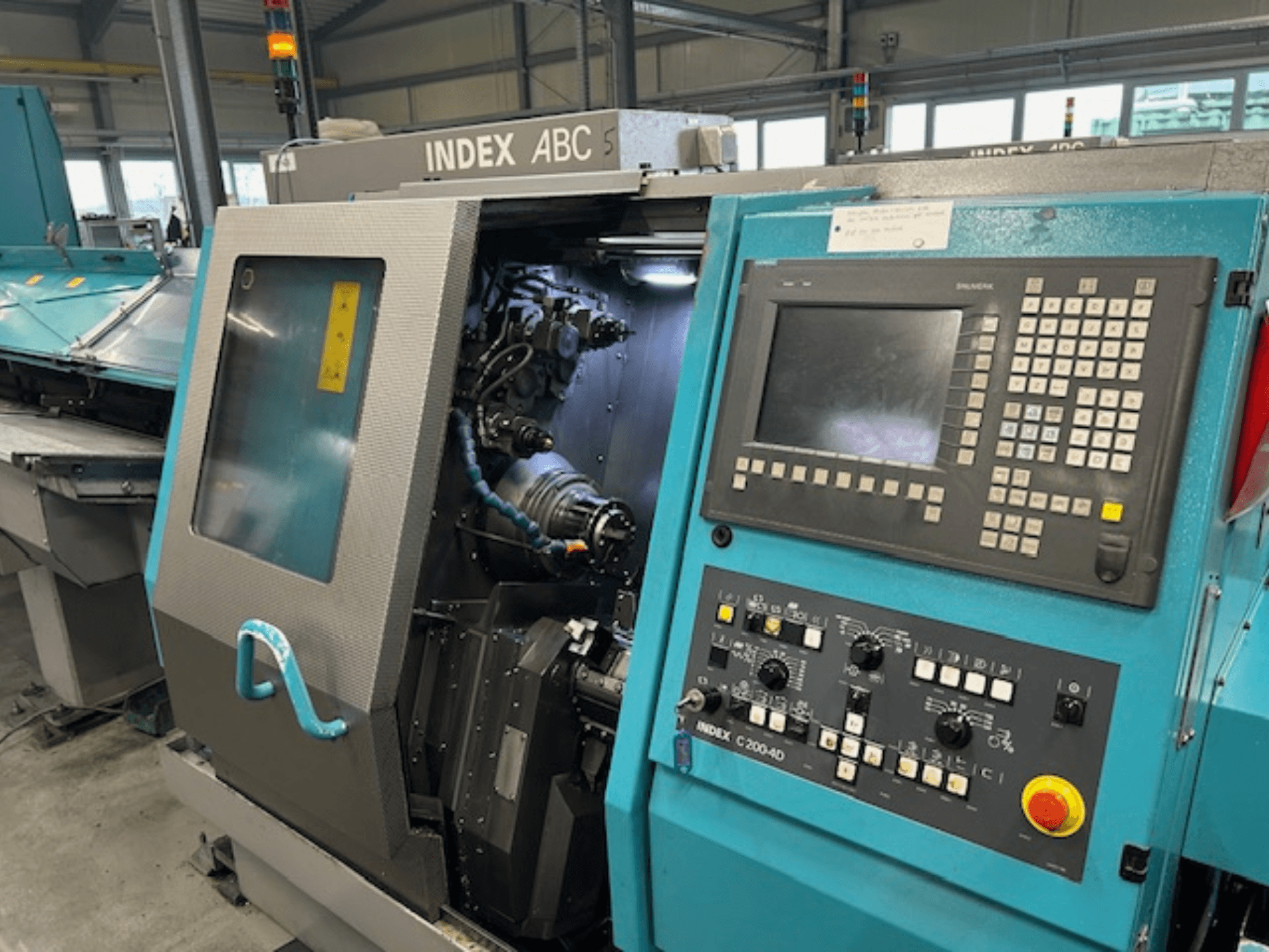 Egy INDEX C200-AD CNC eszterga előlapja a vezérlőpanellel, a látható belső alkatrészekkel és a biztonsági berendezésekkel.