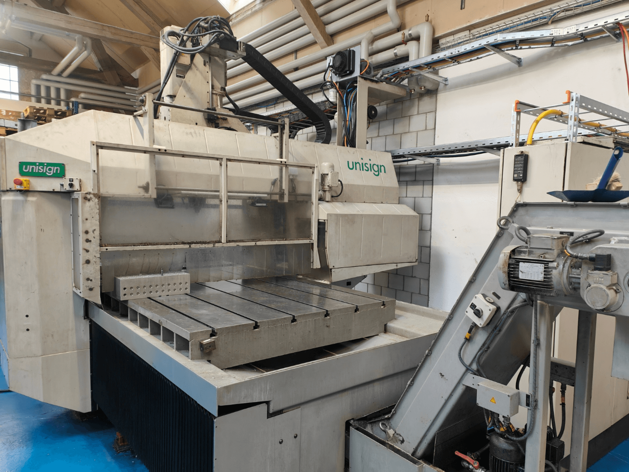 Unisign CNC-gép egy műhelyben, elölnézetben, nagy asztallal, vezérlőpanellel és ipari formatervezési elemekkel.