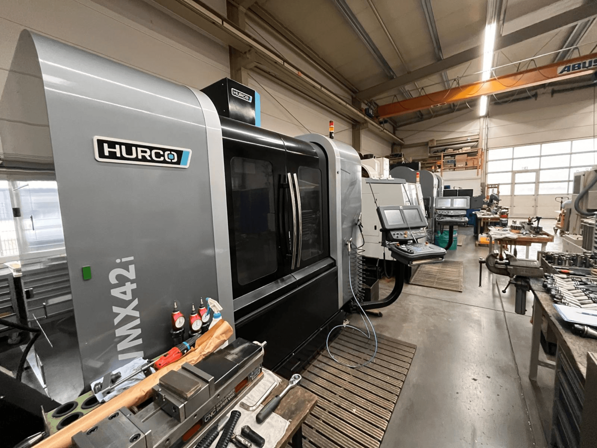 Hurco VMX42i CNC-gép egy műhelyben, elölnézetből. Jellemzők: vezérlőpanel, szürke karosszéria és ipari környezet.