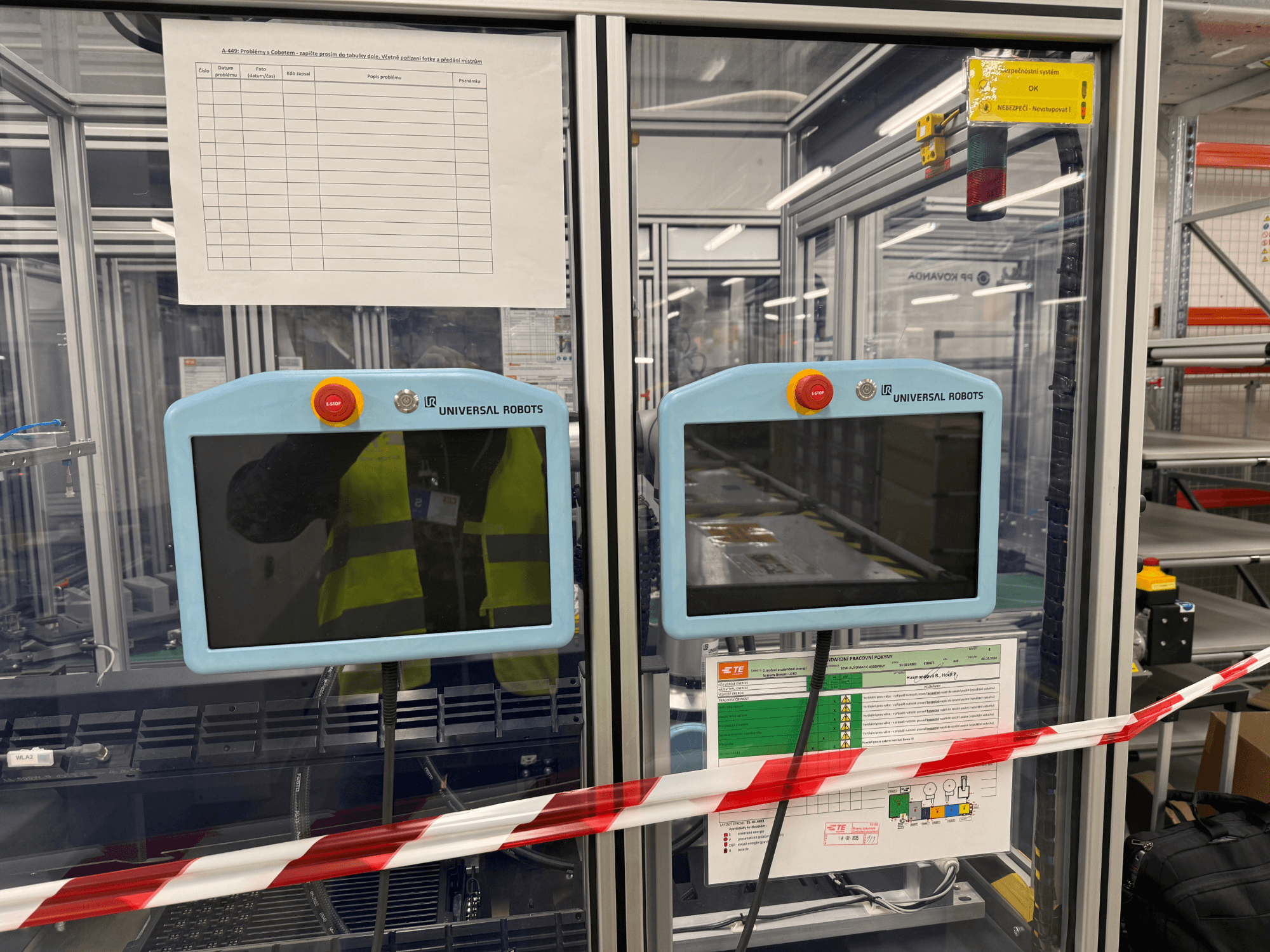 Vezérlőpanel az Universal Robots UR5 e robotkarhoz, két monitorral, vészleállító gombokkal és biztonsági utasításokkal.