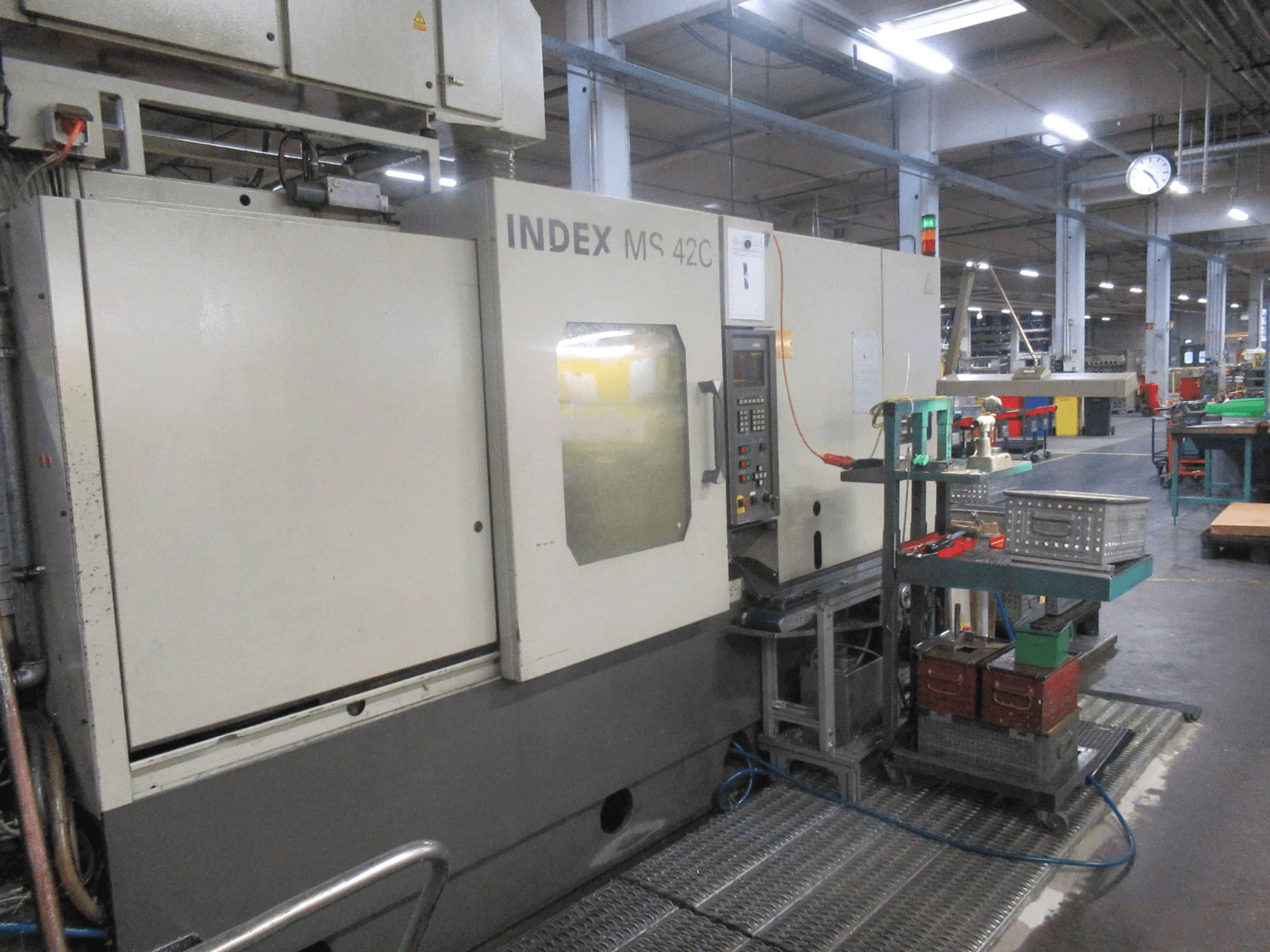 INDEX MS 42C CNC-gép egy műhelyben, oldalnézetben a vezérlőpanel és a szerszámtároló a kerekes kocsin.