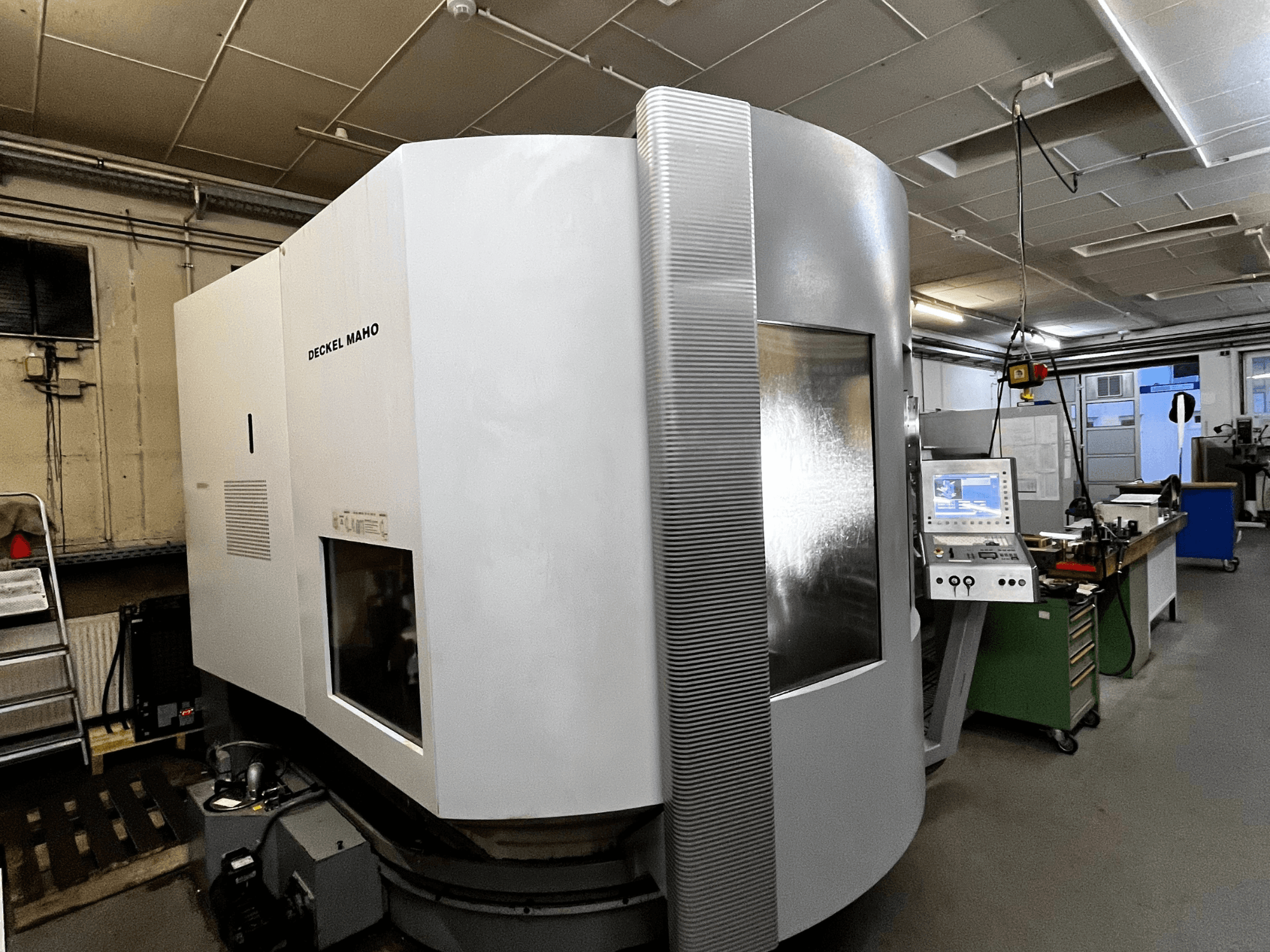 Deckel Maho CNC gép, elölnézet, fehér külső, vezérlőpanel látható, műhelybeállítás.