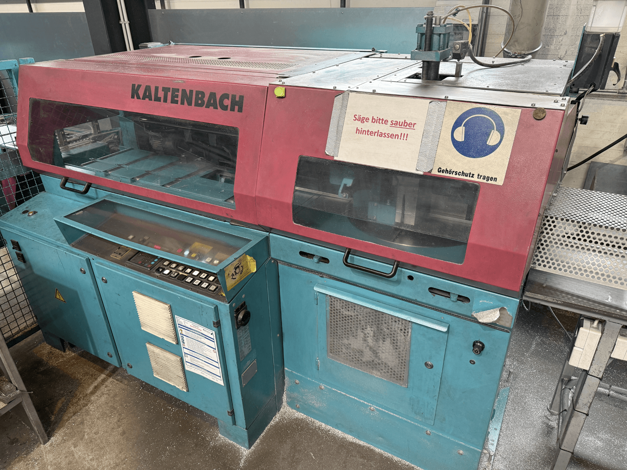 KALTENBACH ipari vágógép, elölnézetben, kezelőpanellel és a hallásvédelmet jelző biztonsági táblával.