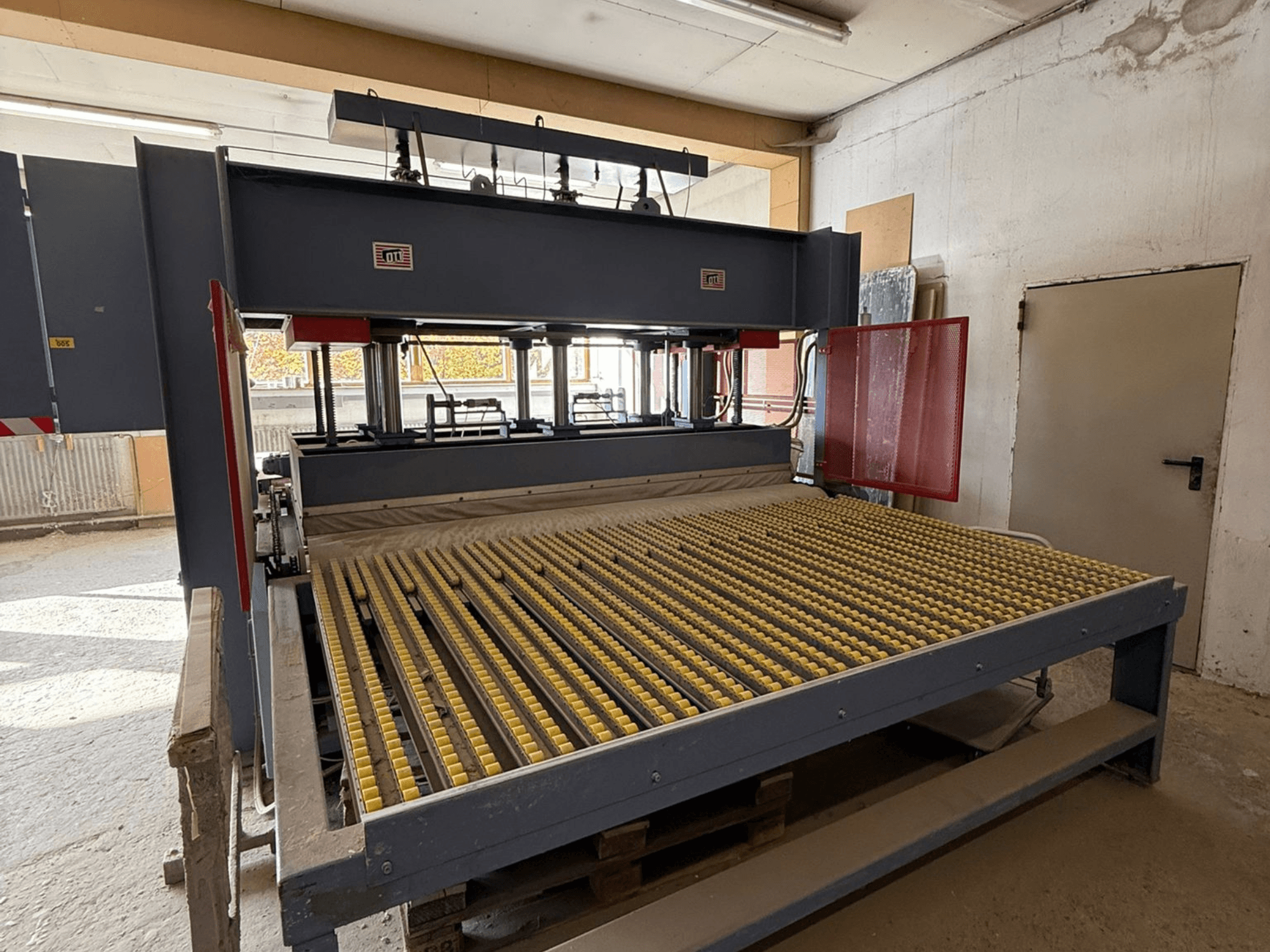 Ipari gép sárga görgőkkel, elölnézetben, a márka logója látható, műhelyben történő anyagfeldolgozásra használják.