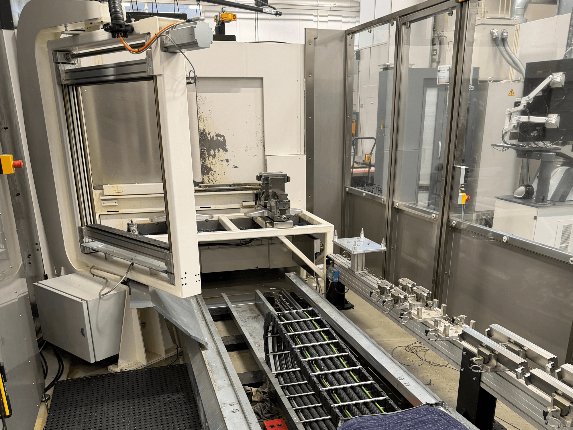 Automatizált ipari munkaállomás, amely oldalnézetben egy robotkart, egy sínrendszert és egy vezérlőpanelt mutat be.