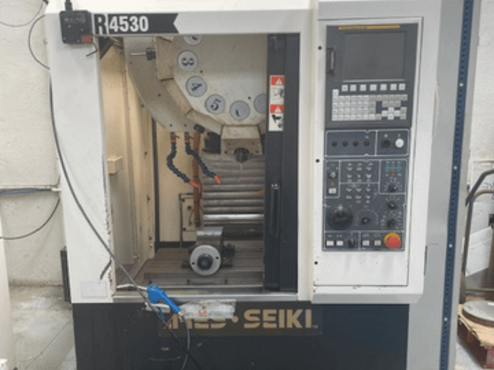 Függőleges megmunkálóközpont ARES-SEIKI R4530, elölnézetben a vezérlőpanel és a munkaterület az orsóval és a hűtőfolyadék-rendszerrel.