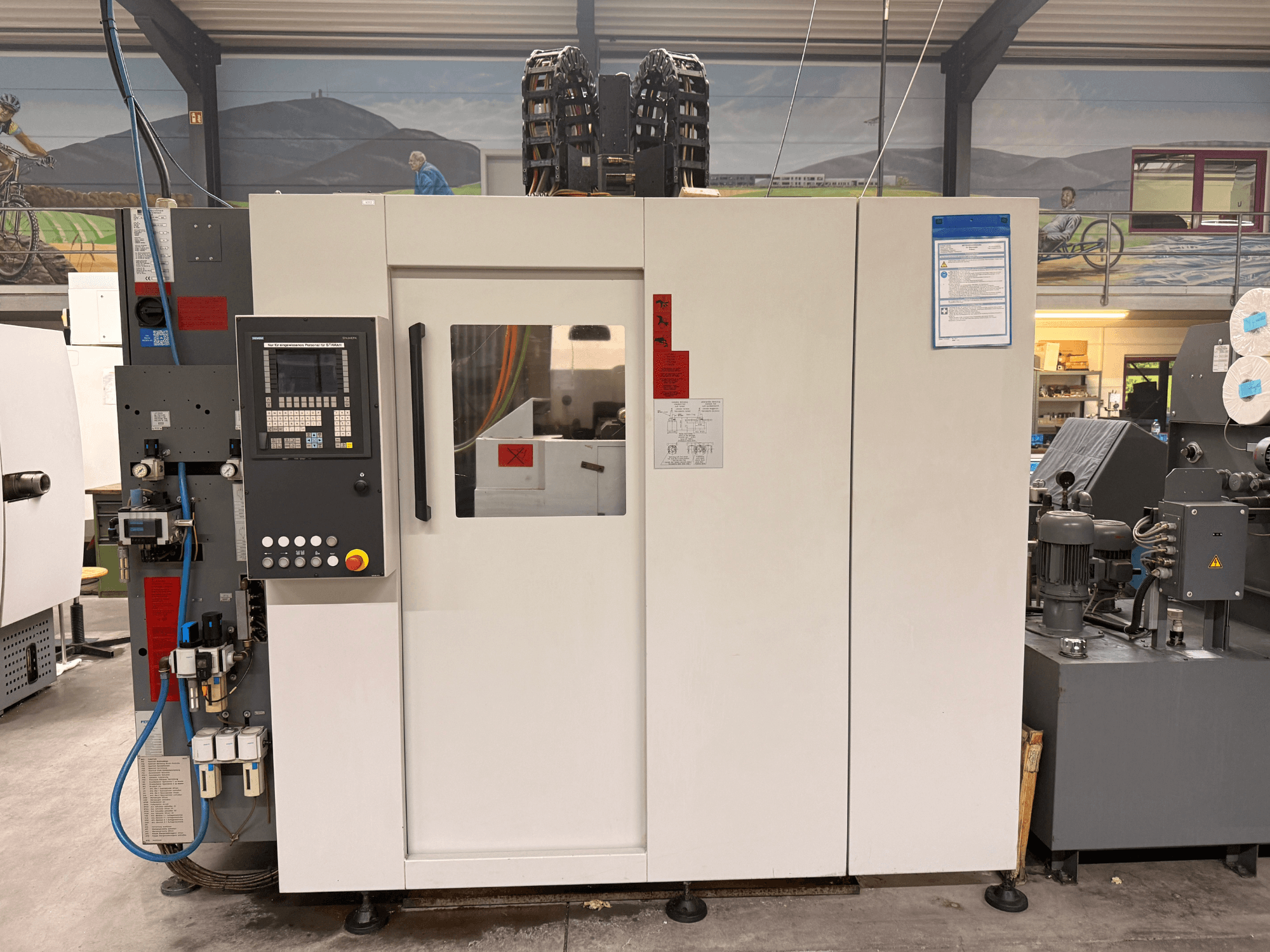 Fehér CNC megmunkálóközpont vezérlőpanellel, elölnézetben, gombokkal és digitális kijelzővel, műhelyben.