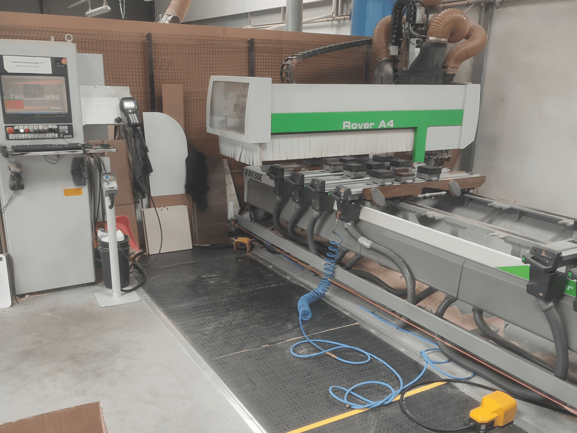 A BIESSE Rover A4 CNC famegmunkáló központ oldalnézete, amelyen látható a vezérlőpanel, a vákuumrögzítők és a porelszívó rendszer.