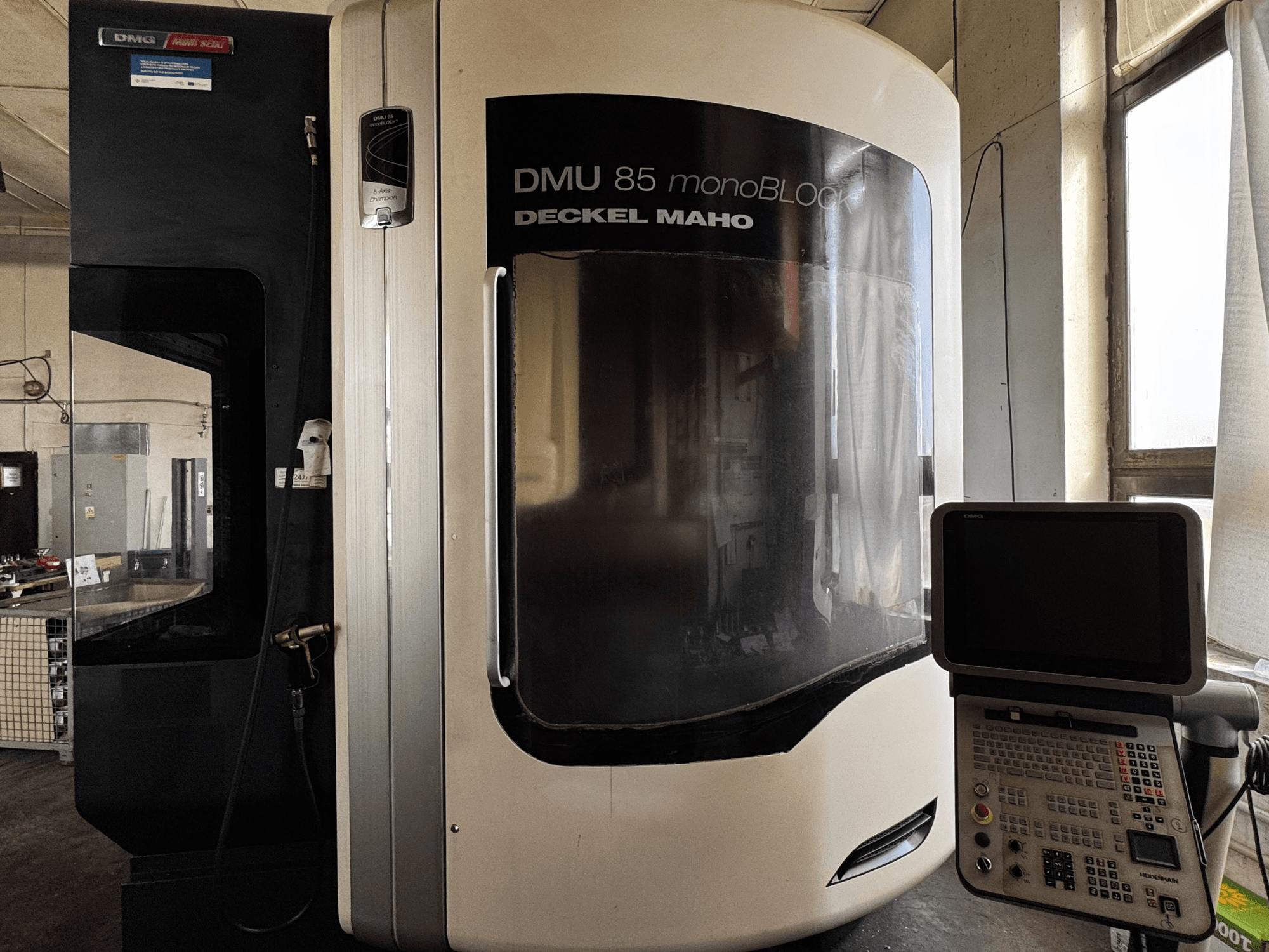 DMG MORI DMU 85 monoBLOCK függőleges megmunkálóközpont, előlnézet a kezelőpanellel és a nagy ablakkal.