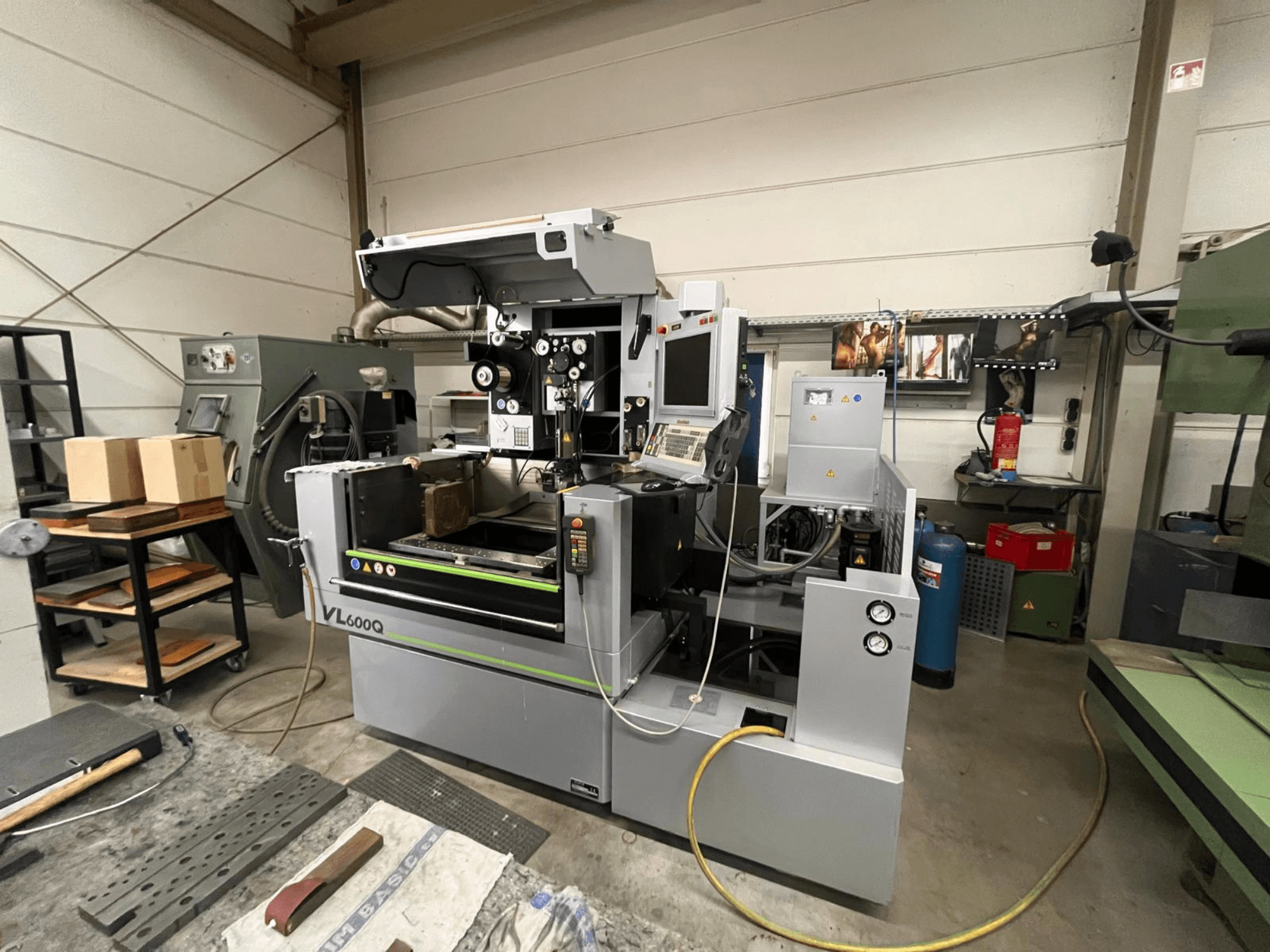 VL600Q CNC-gép egy műhelyben, elölnézetben, kezelőpanellel, a helyére helyezett anyaggal és különböző szerszámokkal a közelben.