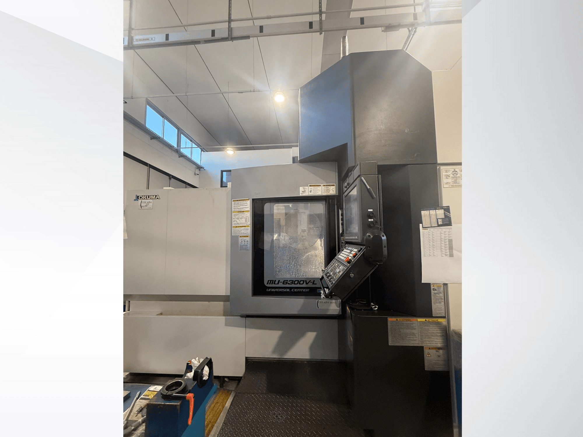Okuma MU-6300V-L CNC-gép elölről, a vezérlőpanel és a biztonsági címkék bemutatásával.