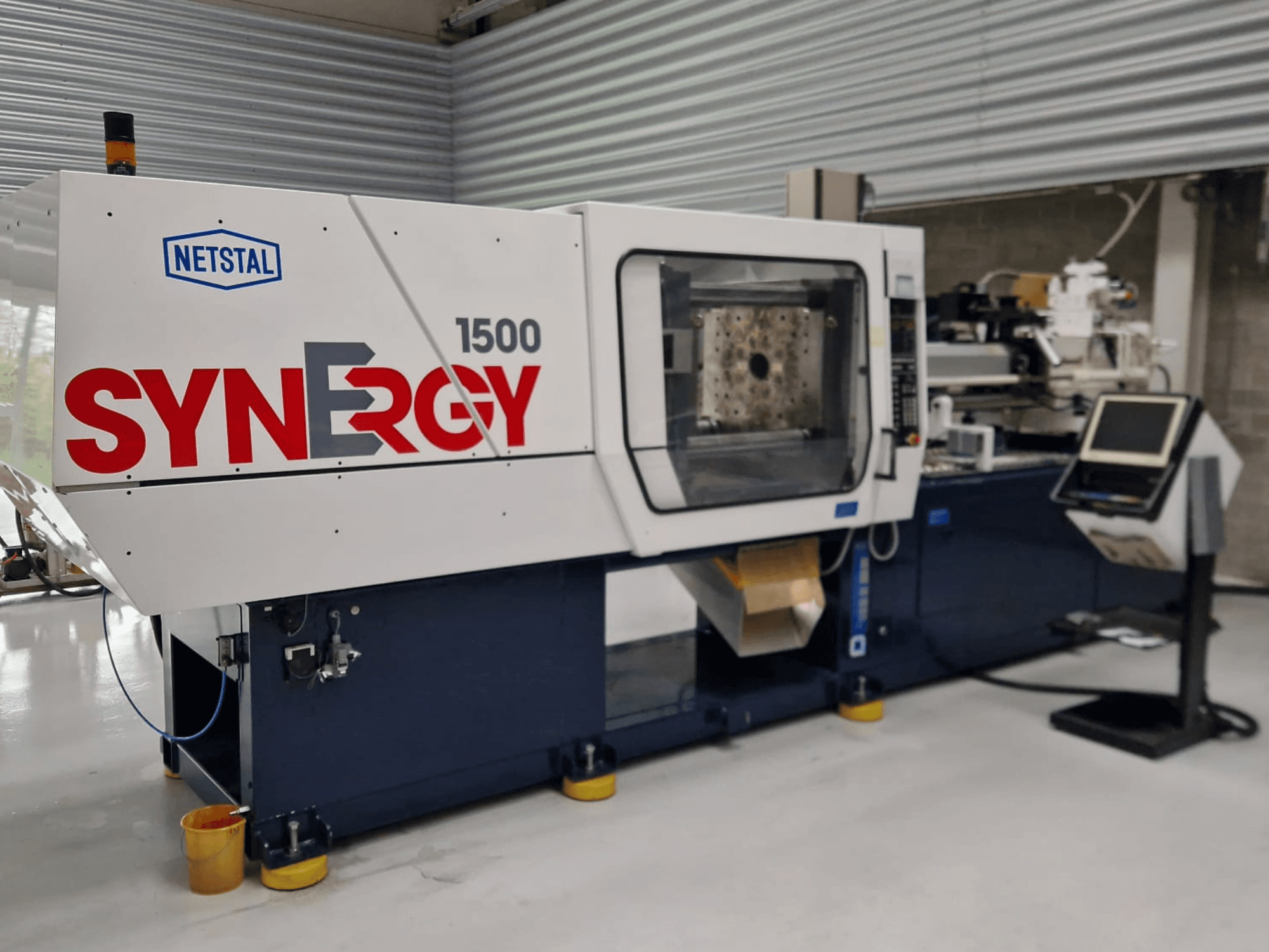 Netstal Synergy 1500-460 hidraulikus fröccsöntőgép, elölnézetből, a vezérlőpanel és a nyitott fröccsöntési terület bemutatásával.