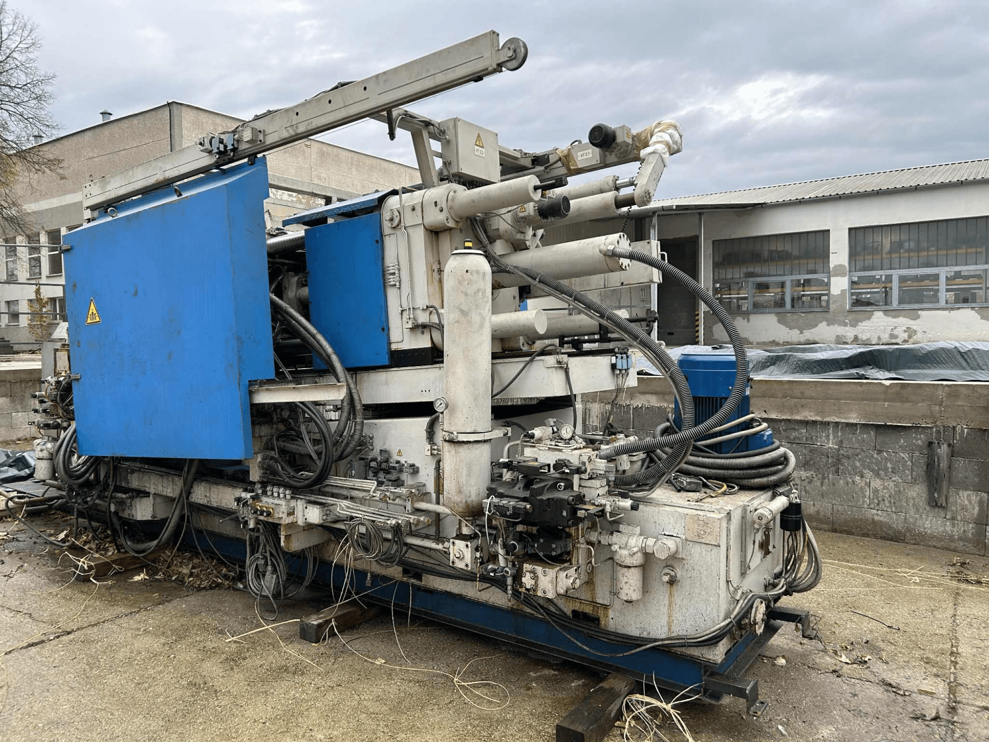 Nagy ipari hidraulikagép kék burkolattal, különböző tömlőkkel és fém alkatrészekkel, oldalról nézve.