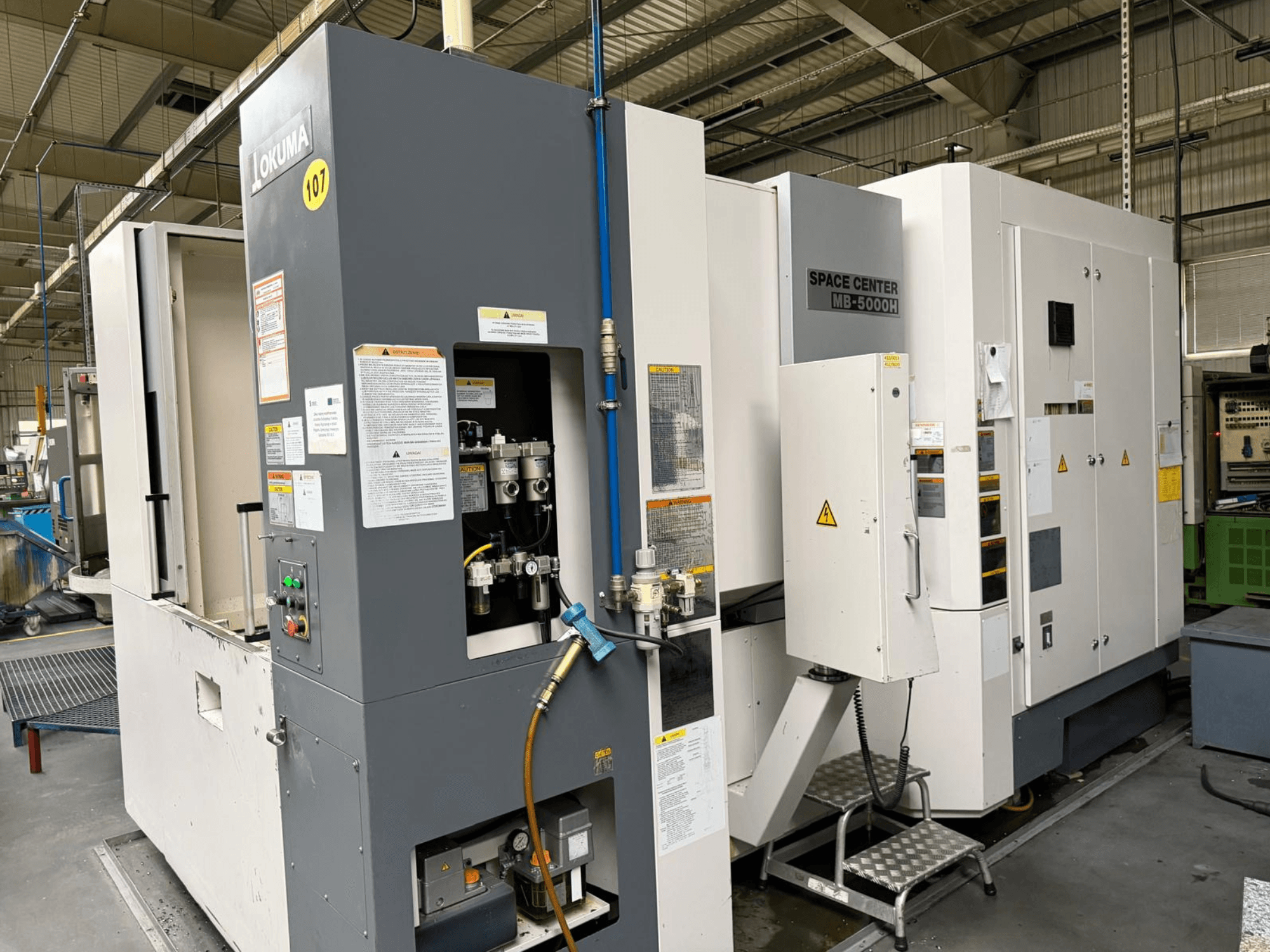 Okuma MB 5000H vízszintes megmunkálóközpont, oldalnézet a vezérlőpanel és a gépelemek bemutatása gyári környezetben.