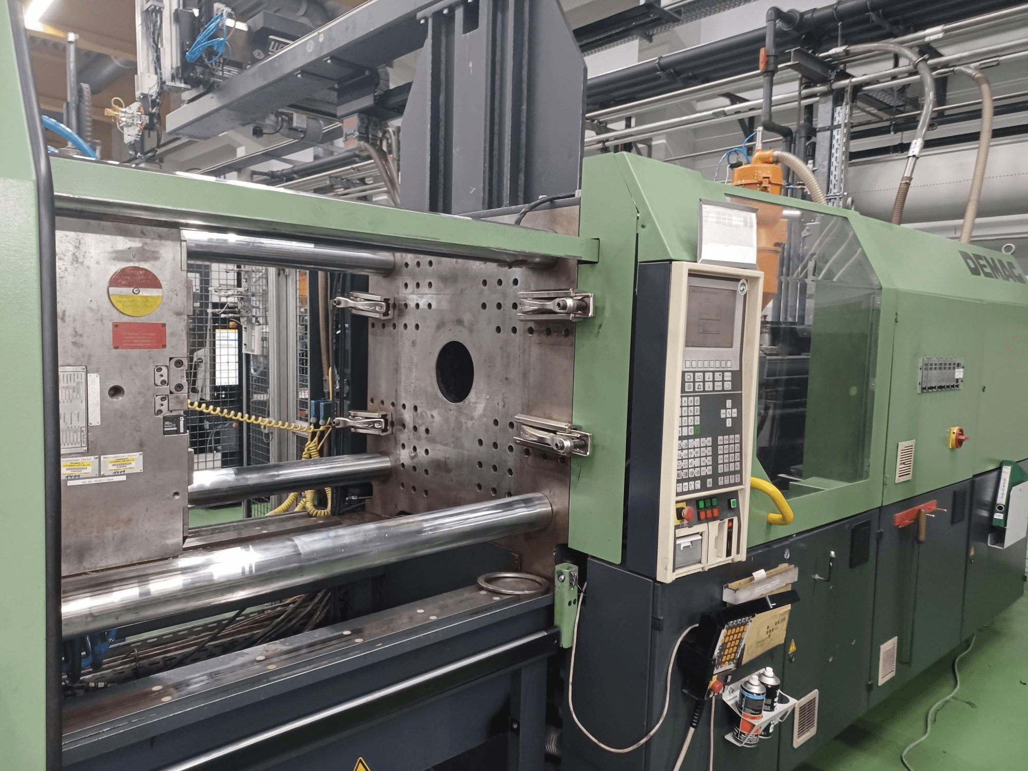 Demag fröccsöntőgép, elölnézet, vezérlőpanel, fém hidraulikus hengerek és biztonsági berendezések.