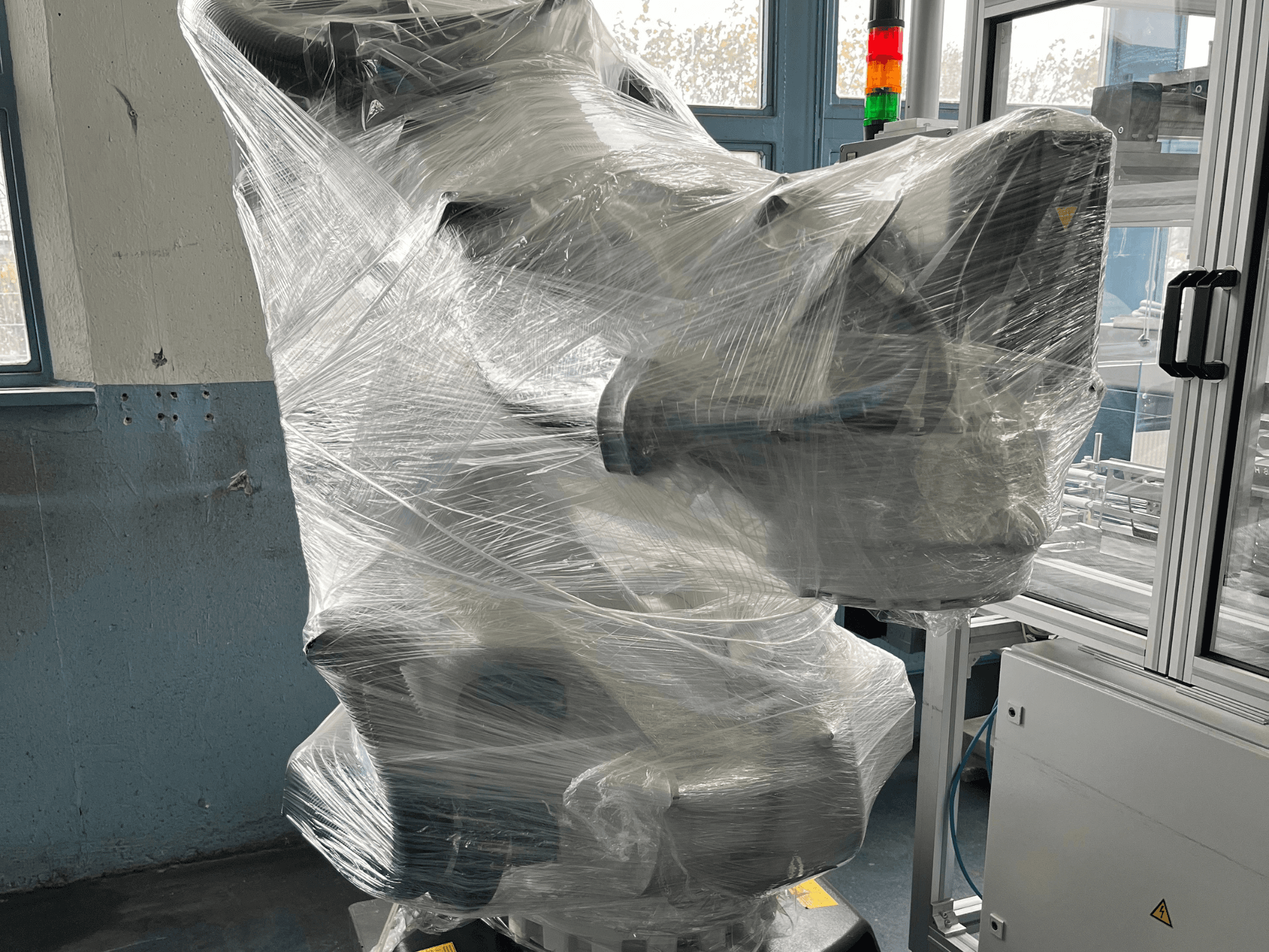 Ipari robotkar műanyagba csomagolva, elölnézet. Tartalmazza a vezérlőegységet és a jelzőlámpát. Márka nem látható.