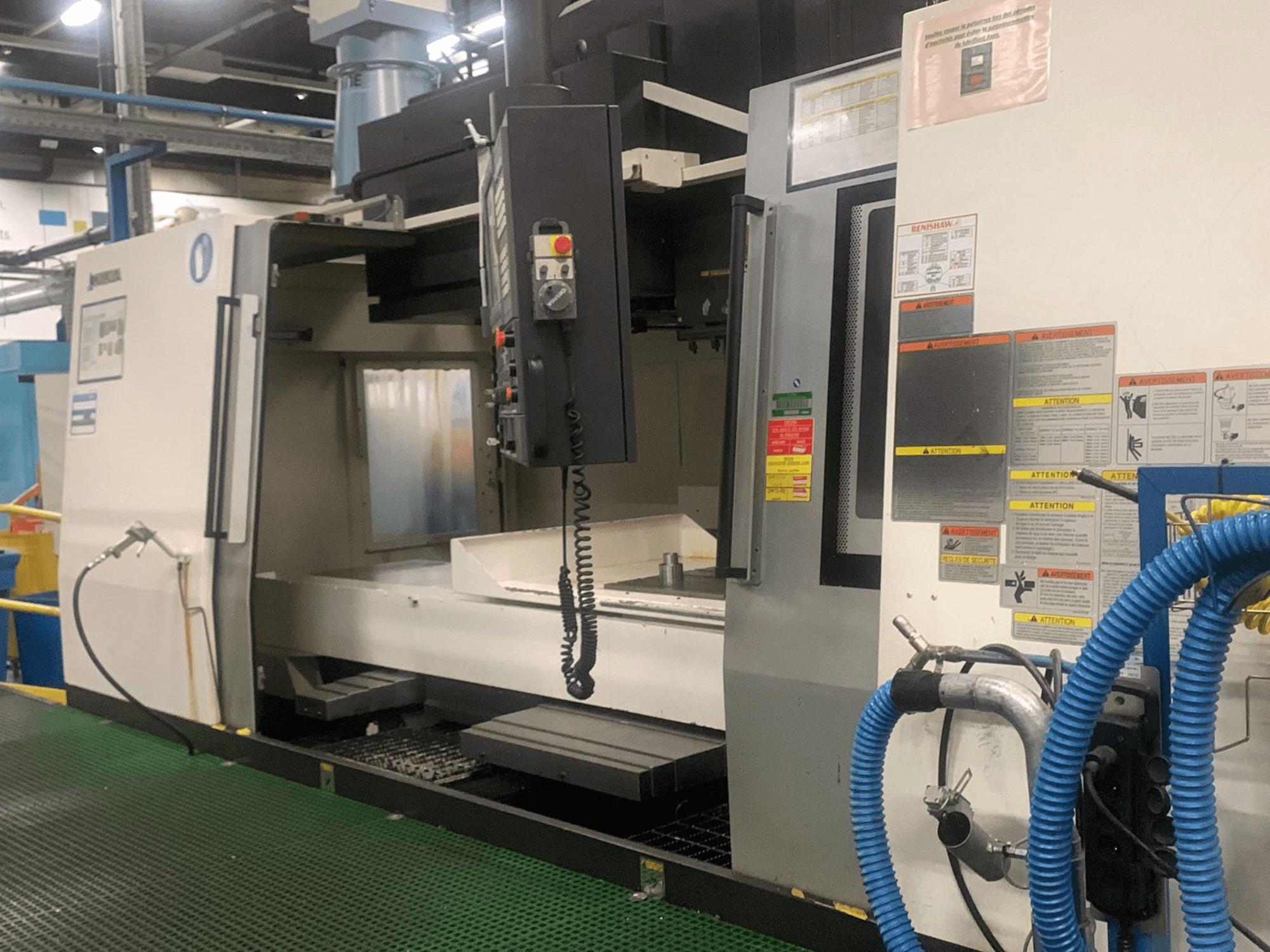 Okuma Millac 852 VII függőleges megmunkáló központ, elölnézet, amelyen látható a vezérlőpanel, az orsóterület és a biztonsági címkék.