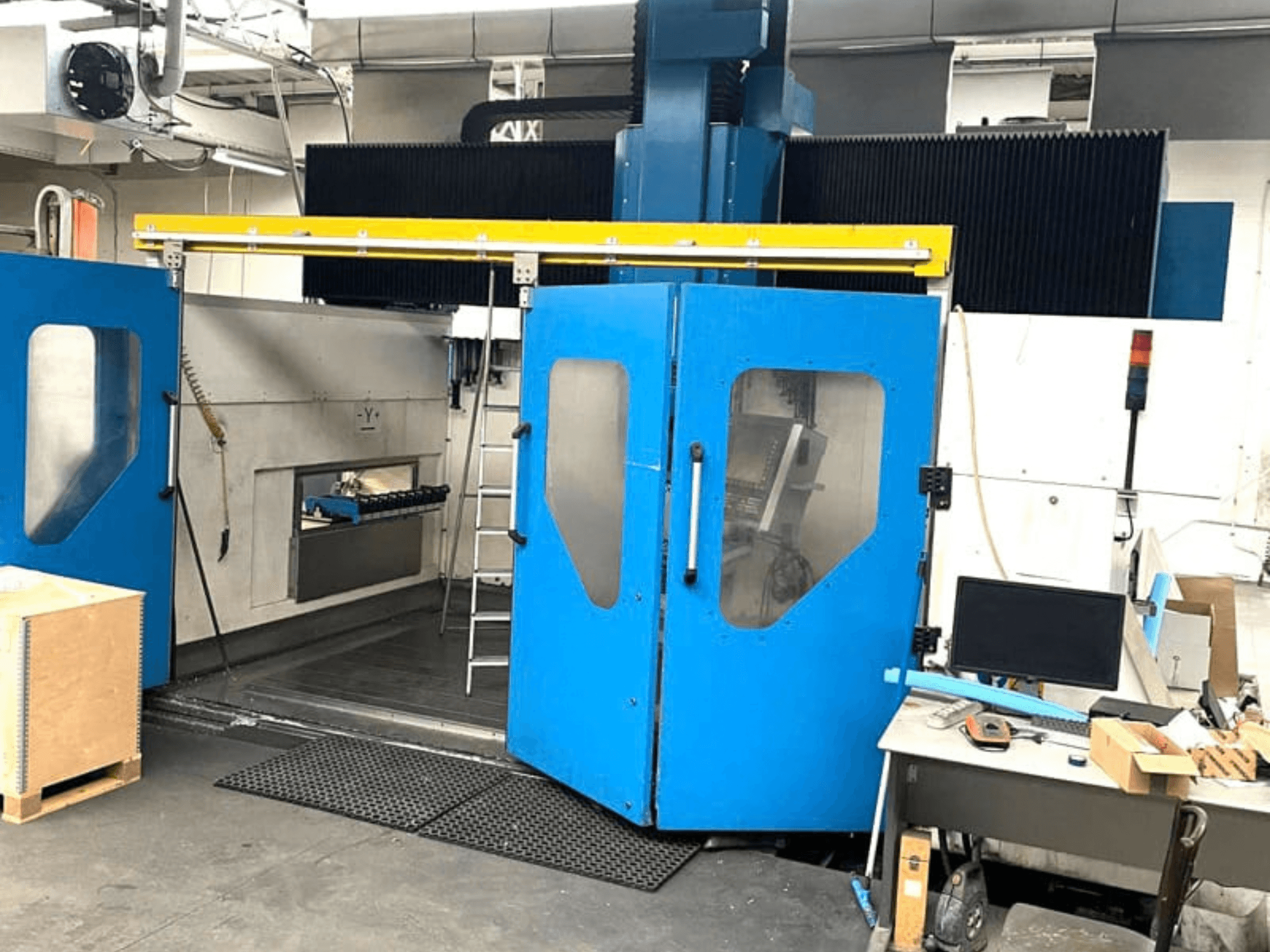 A TECHMILL LABOR SHAPE 3220 függőleges megmunkáló központ elölnézete, kinyitott kék ajtókkal, amelyekből látható a belső munkaterület.