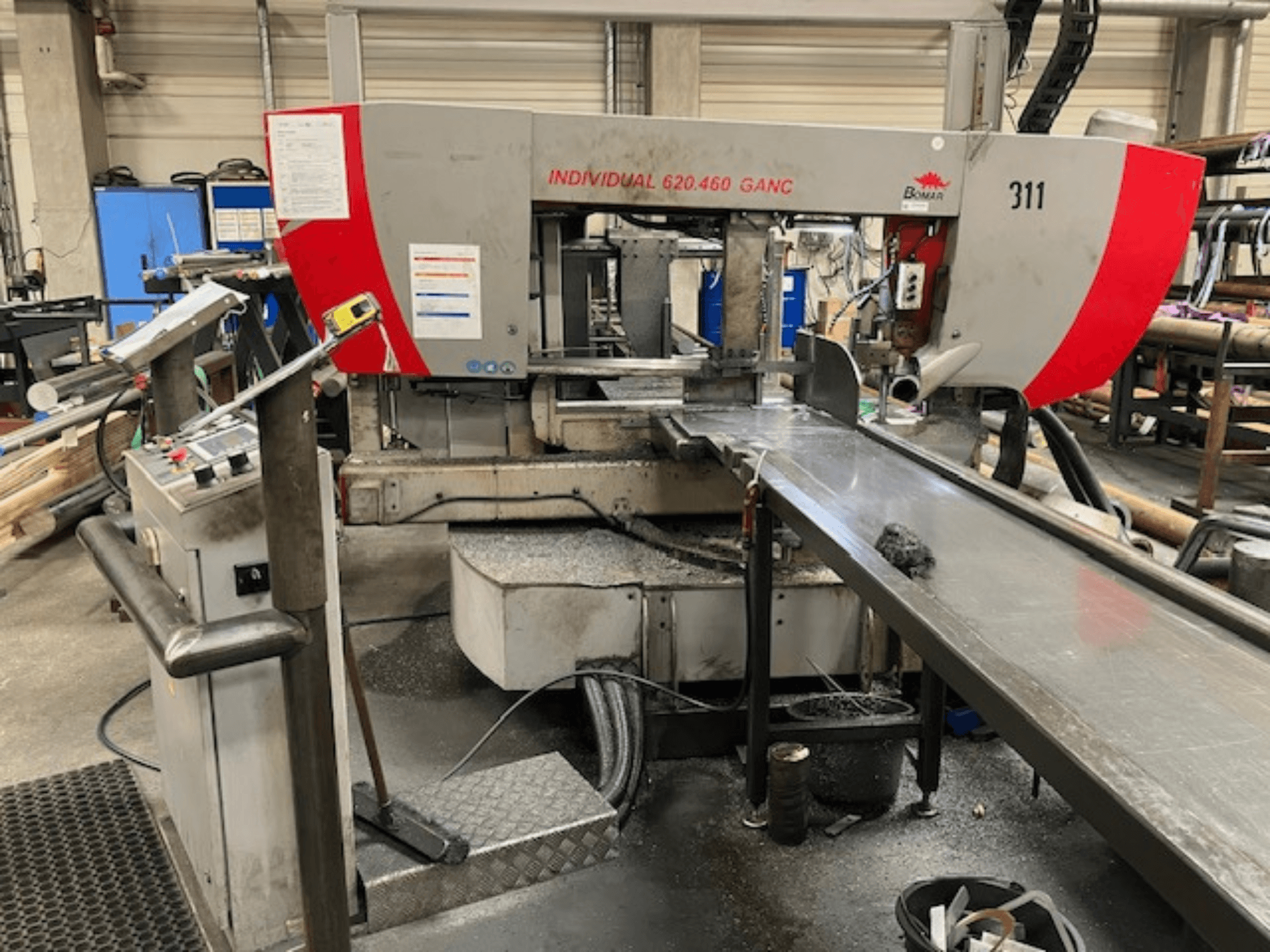 BOMAR INDIVIDUAL 620-460 GANC szalagfűrész, elölnézet, a kezelőszervek, a vágási terület és az ipari műhely háttere.