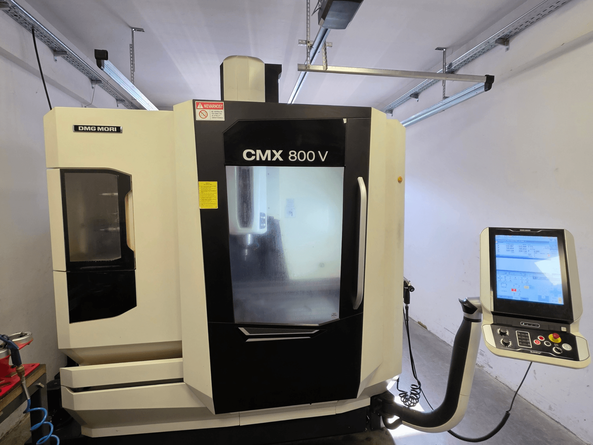 DMG MORI CMX 800V függőleges megmunkáló központ, elölnézet, érintőképernyős vezérlőpanellel és jól látható biztonsági jelzésekkel.