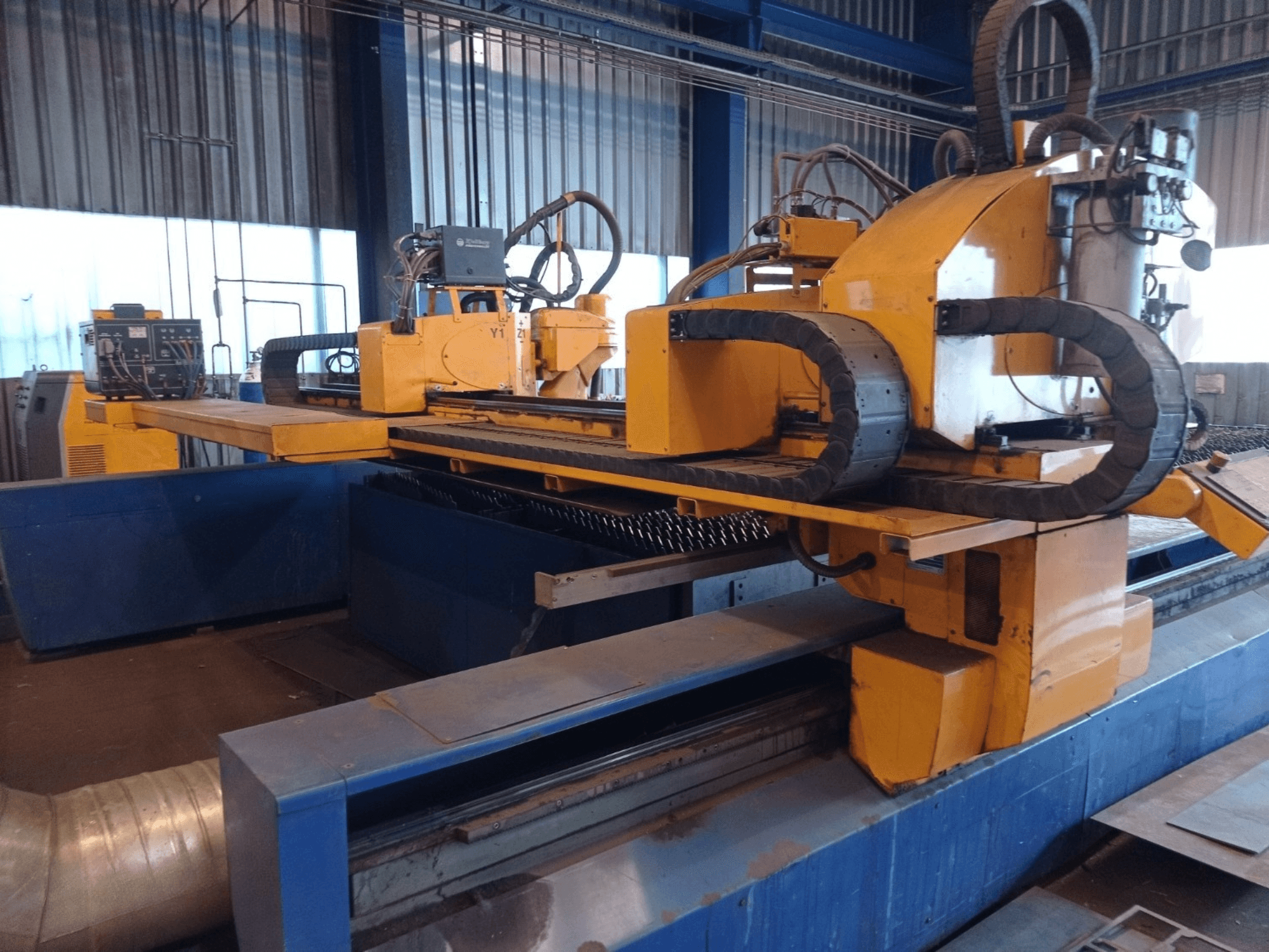 Sárga színű CNC plazmavágó gép két vízszintes karral, szemből, vezérlőpanellel és vágóasztallal.