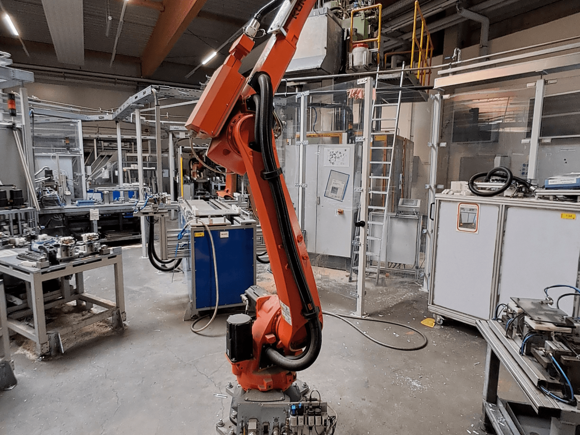 A KUKA KR 26 R3100/SEL robotkar ipari környezetben, oldalnézetből, a háttérben működő berendezésekkel.