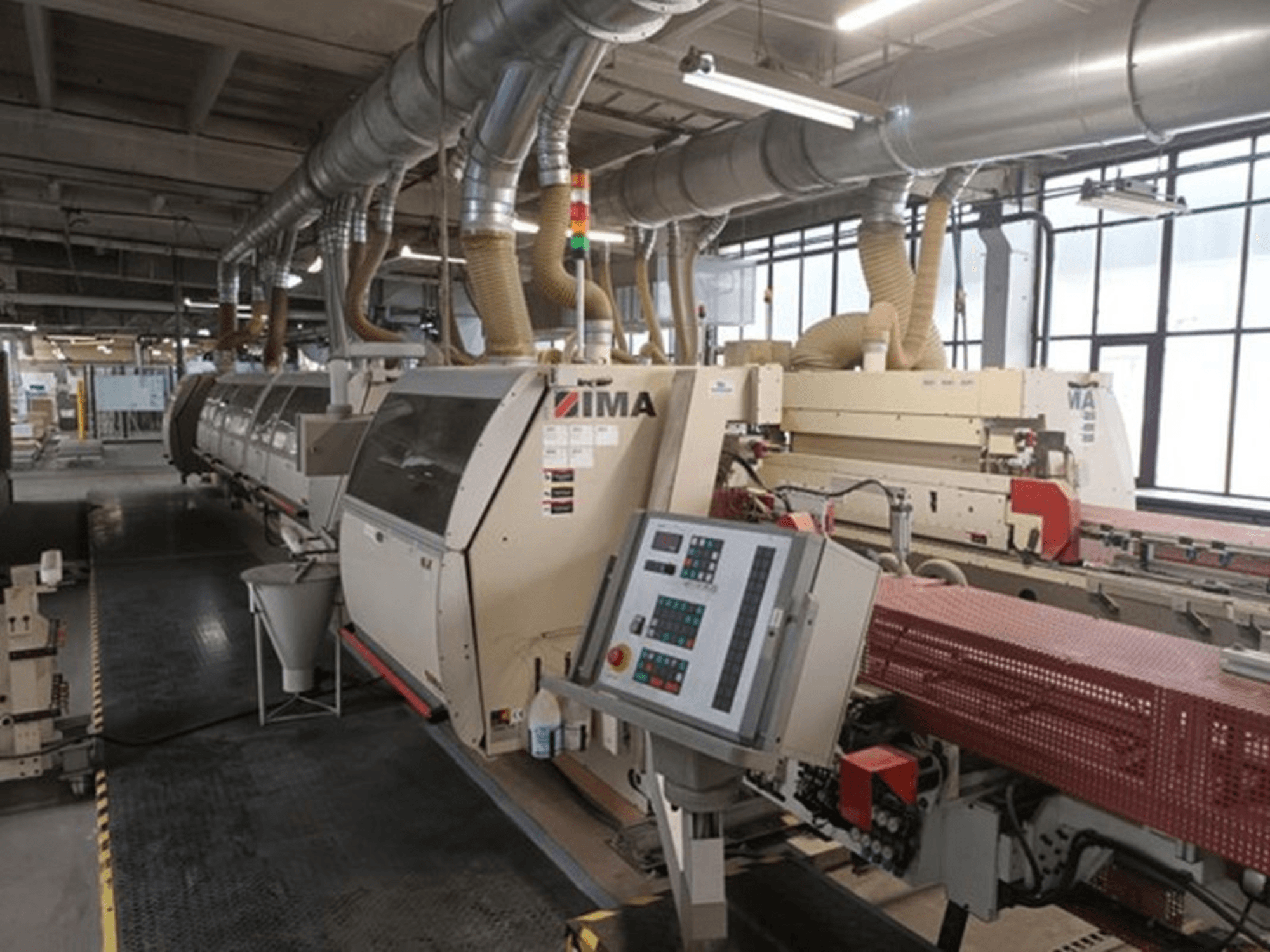 IMA ipari gépek gyári környezetben, elölnézetben, vezérlőpanelekkel és porelszívó csövekkel.