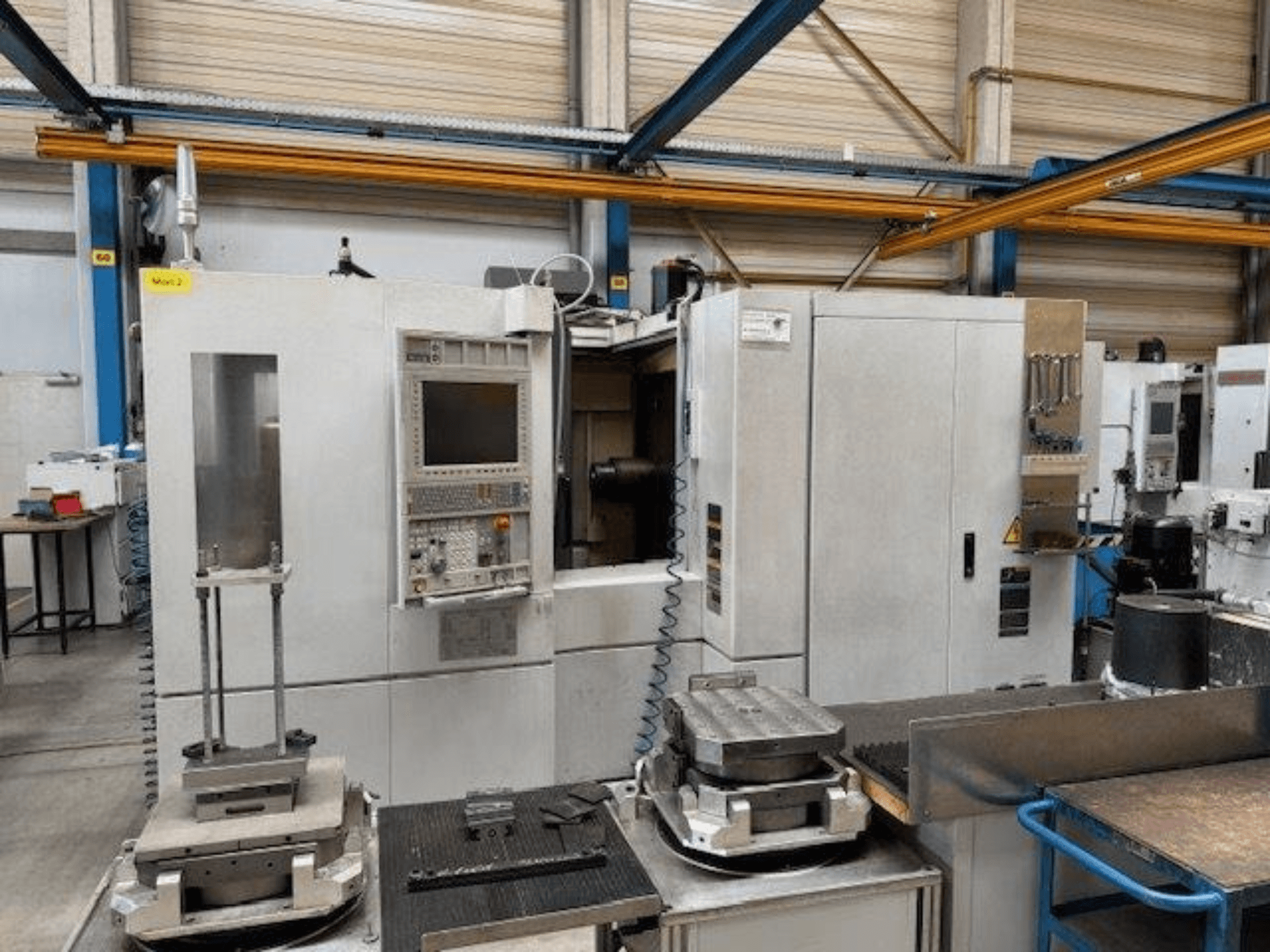 MORI SEIKI NH4000 DCG vízszintes megmunkálóközpont előlapja a vezérlőpanellel és az asztalon lévő munkadarabokkal.