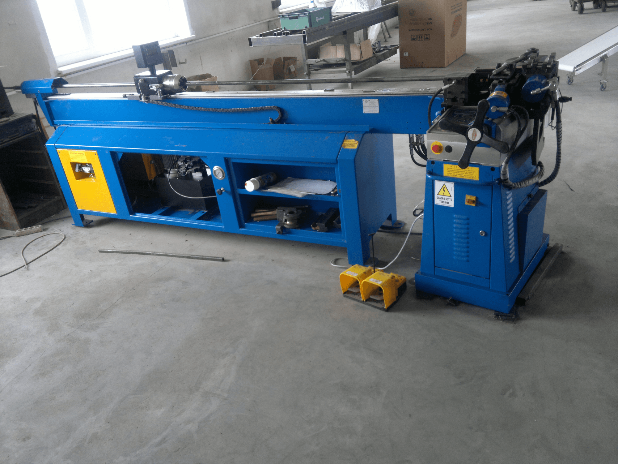 Kék színű, sárga színű famegmunkáló gép oldalnézetben; vezérlőpanellel, lábpedálokkal és forgó pengékkel rendelkezik.