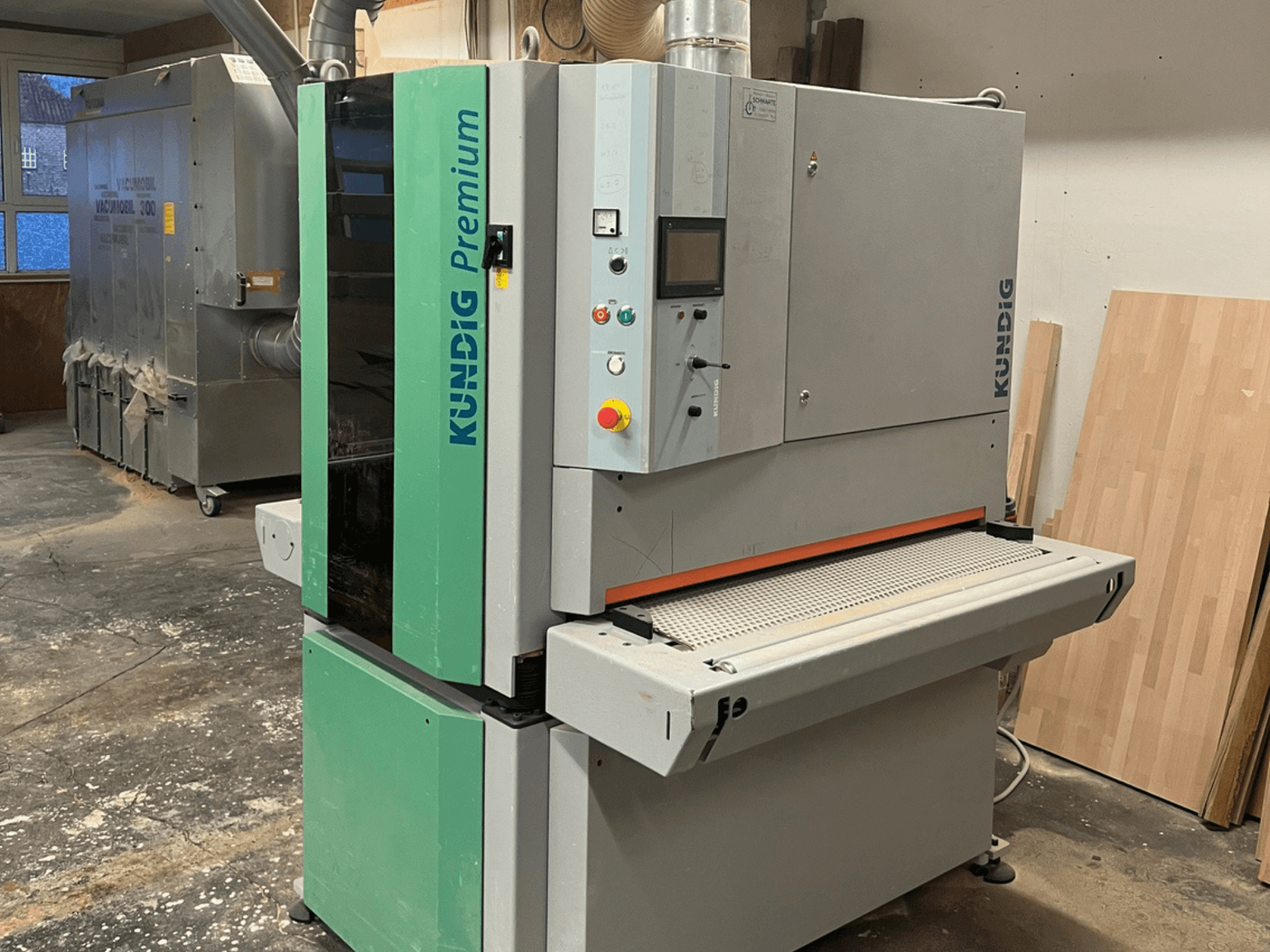 Kundig Premium-1 1100K szalagcsiszoló szürke és zöld színben, oldalnézetben, a vezérlőpanel és a csiszolószalag látható.