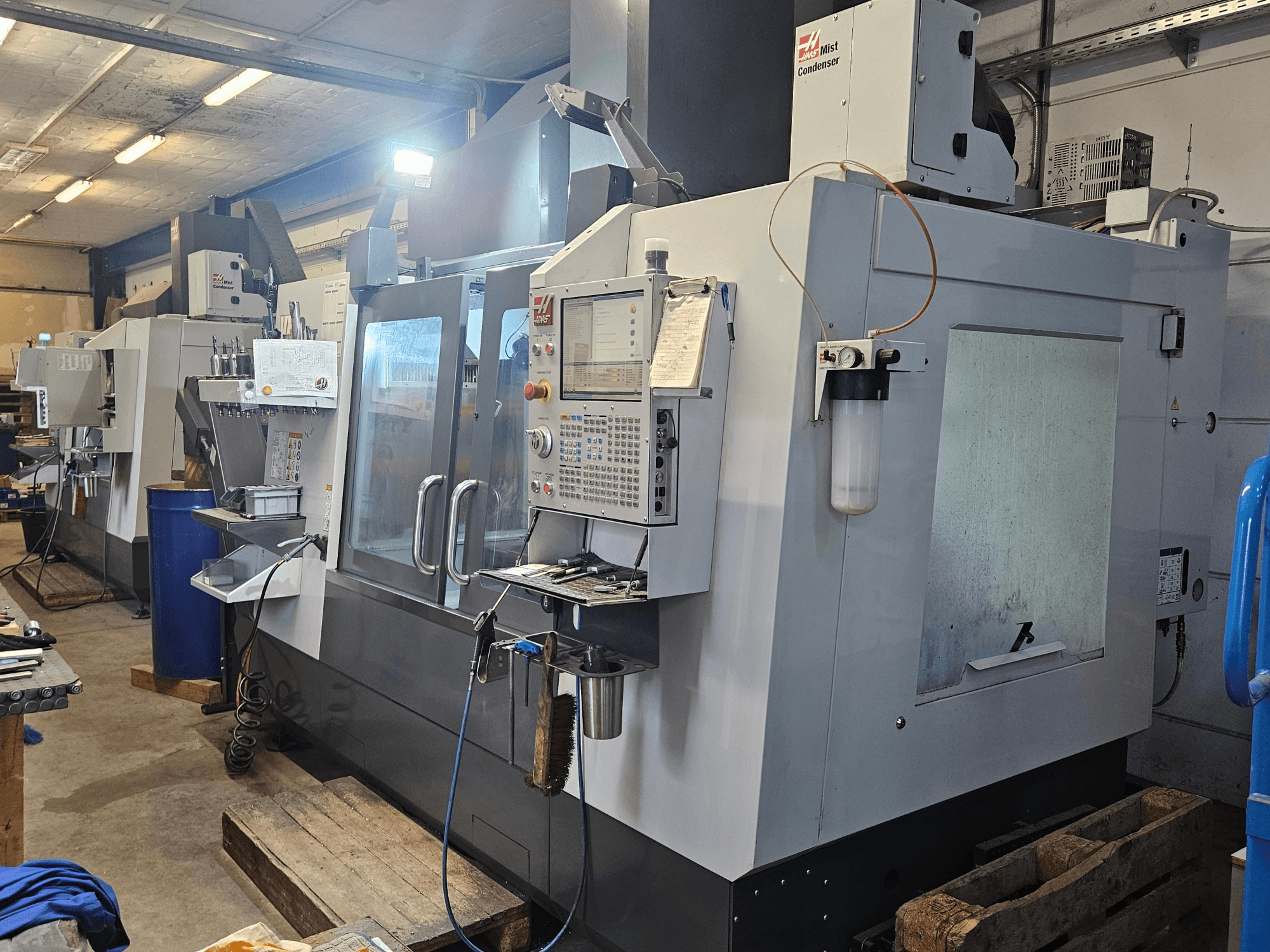Haas VF-3YT/50 függőleges megmunkáló központ egy műhelyben, elölnézetből, amelyen látható a vezérlőpanel, a szerszámtartók és a ködkondenzátor.