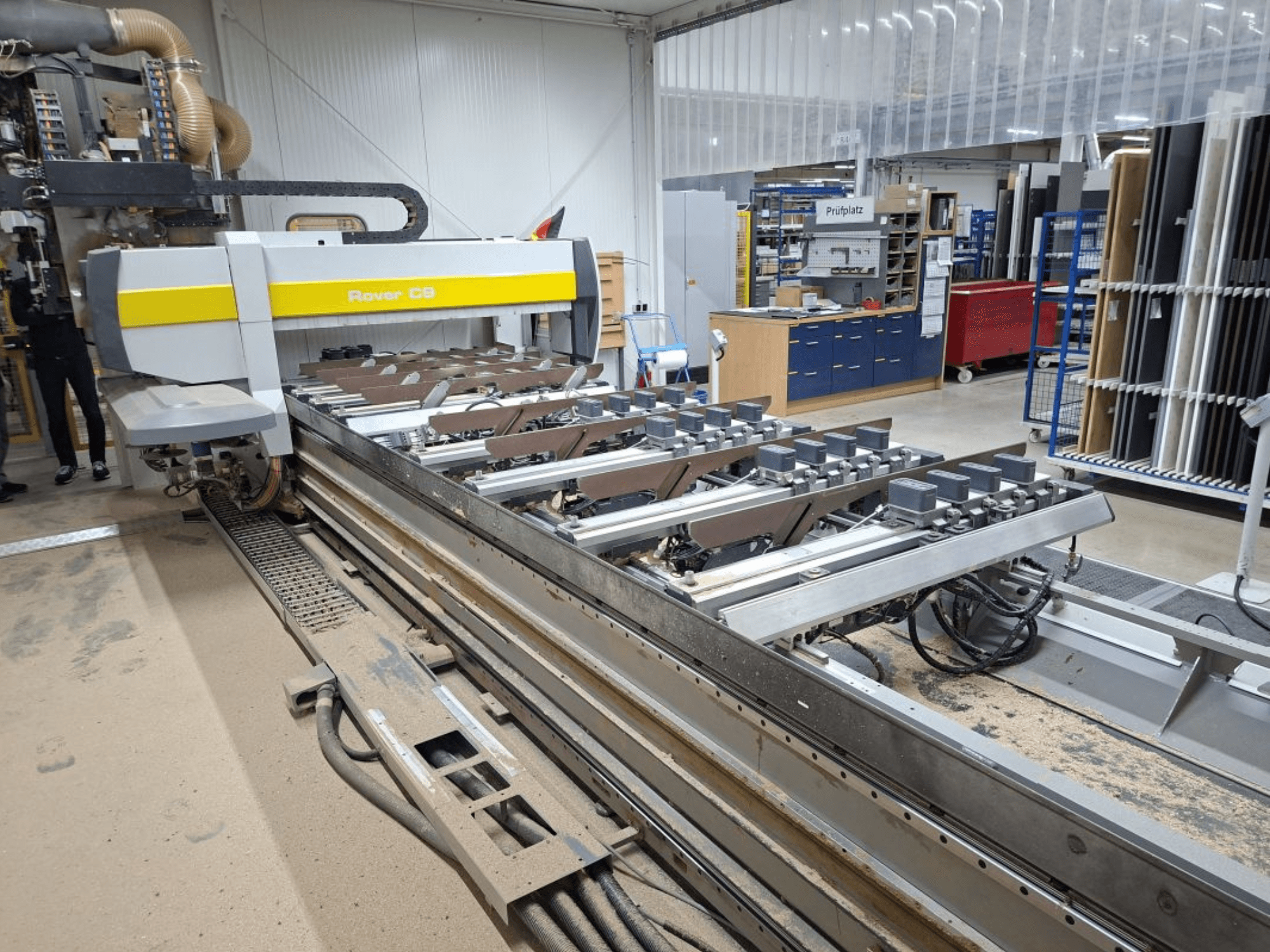 Rover C9 CNC-gép egy műhelyben; elölnézetben a vágószerszámok és a szállítórendszer, a padlón felgyülemlett porral.