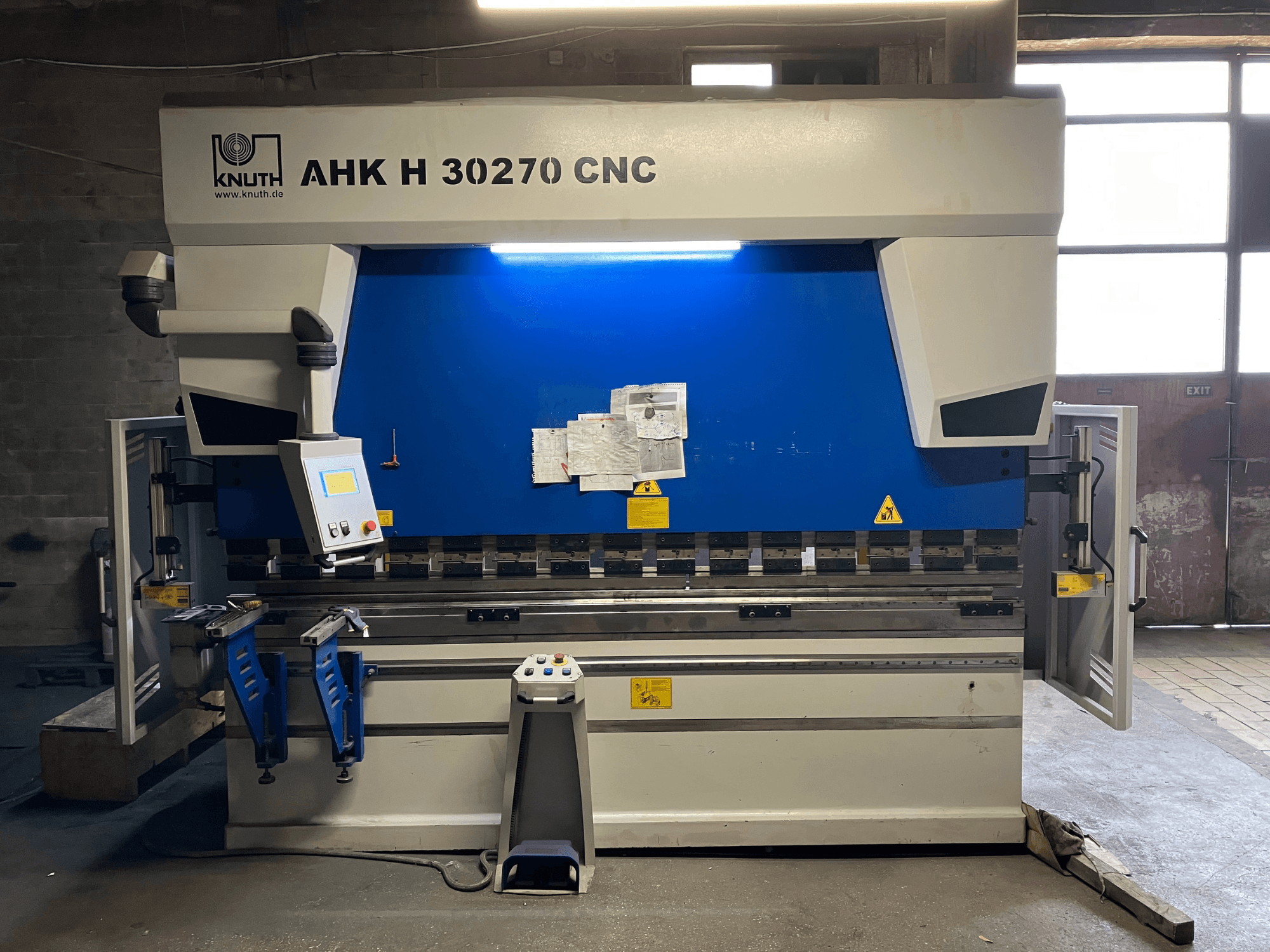 KNUTH AHK H 30270 CNC-s hajlítógép egy műhelyben, elölnézetből, a vezérlőpanellel és a kék-fehér kialakítással, nyitott oldalsó ajtóval.