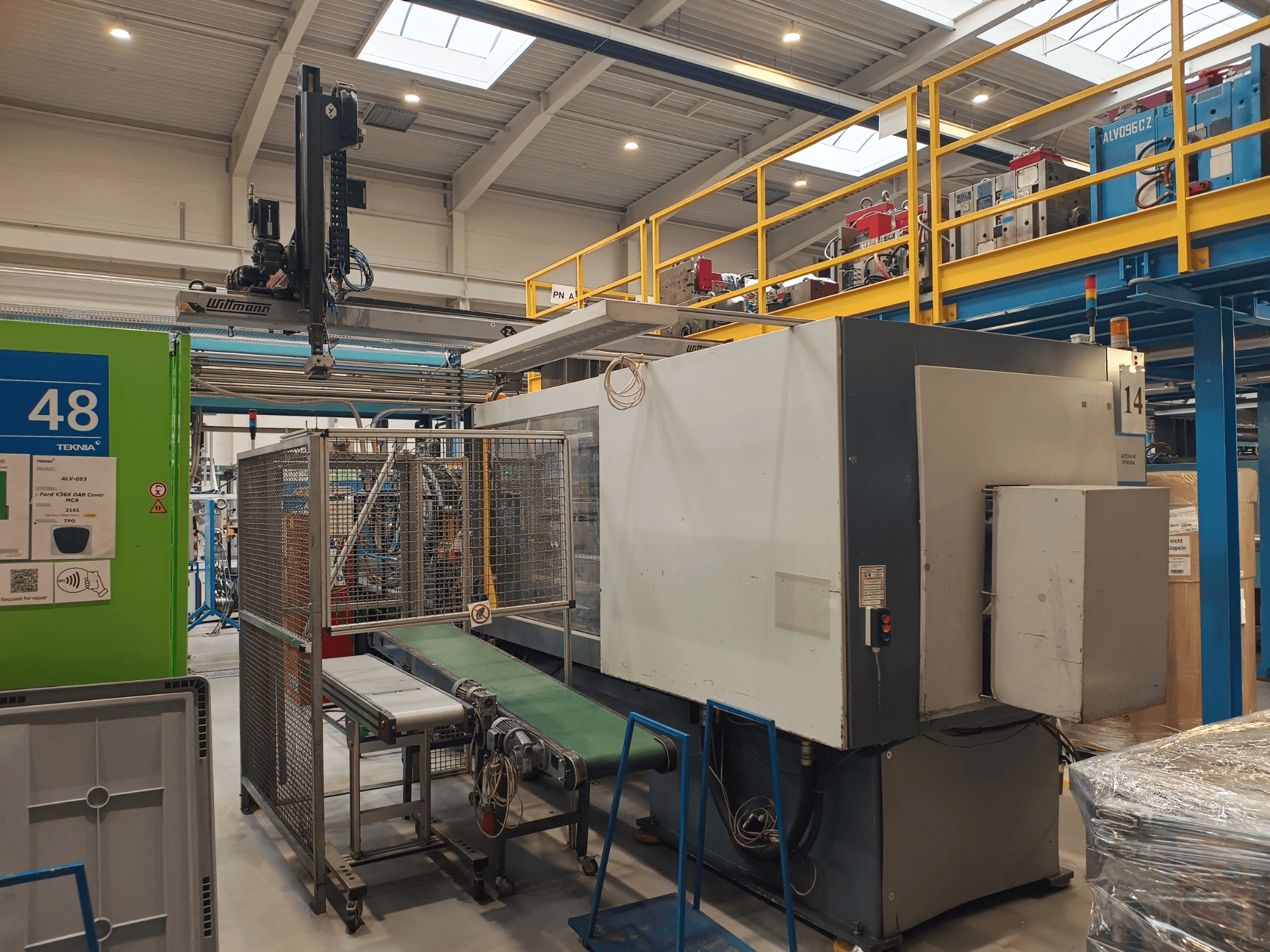 Ipari automatizálási gép a Winmon-tól, oldalnézetben a szállítószalag, a vezérlőpanel és a biztonsági ketrec egy gyári környezetben.