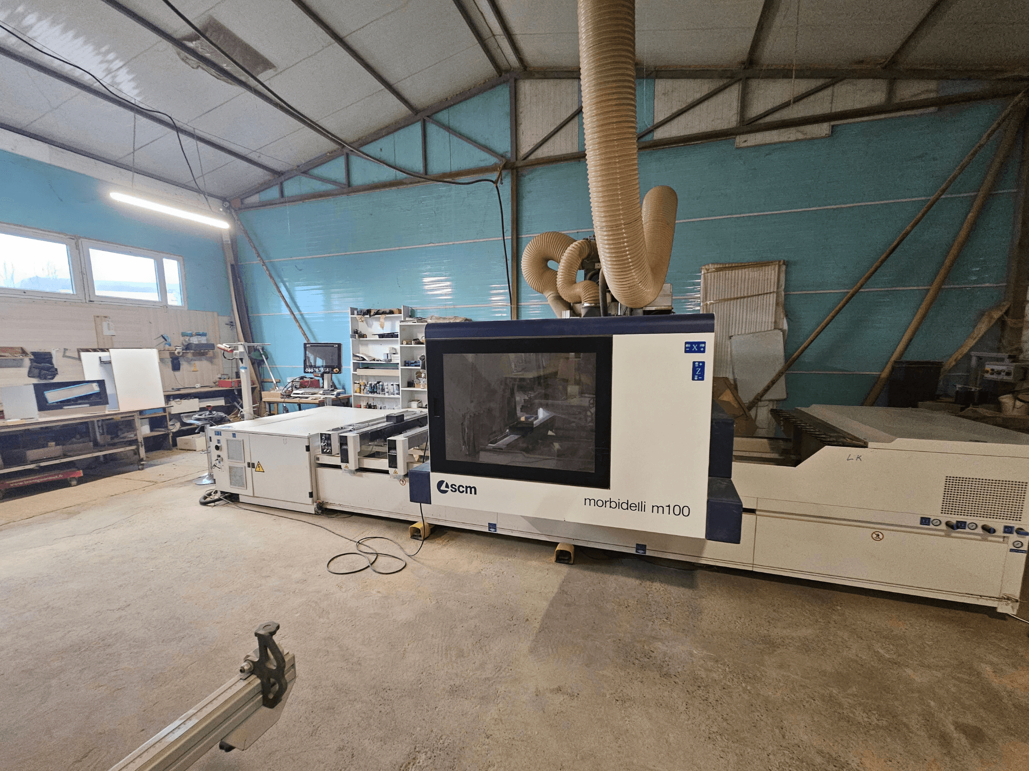 SCM Morbidelli M100 CNC-gép egy műhelyben, elölnézetben, a porelszívó rendszer és a vezérlőpanel bemutatásával.