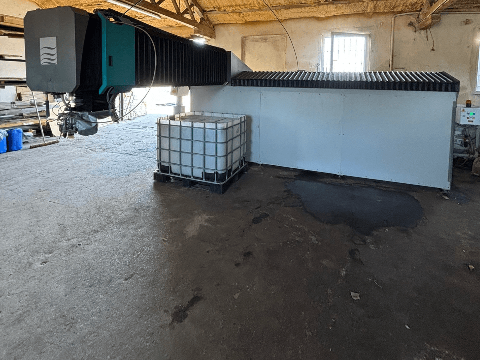 Ipari vízsugaras gép egy műhelyben, oldalnézetben, mellette látható a nagy víztartály és a vezérlőpanel.