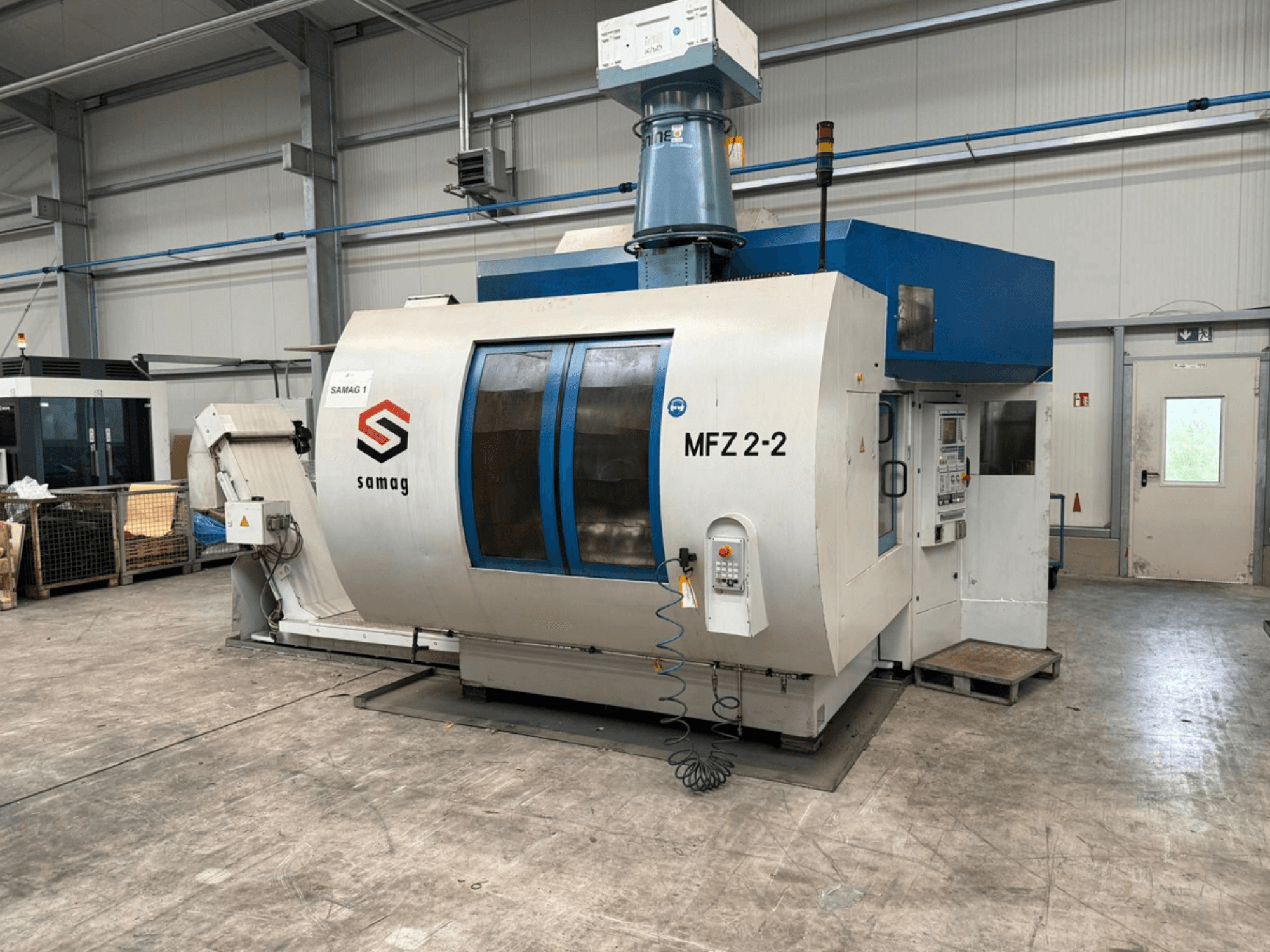 Samag MFZ 2-2 szerszámgép, elölnézet, a vezérlőpanel és a kék felső rész látható, biztonsági berendezésekkel ipari környezetben.