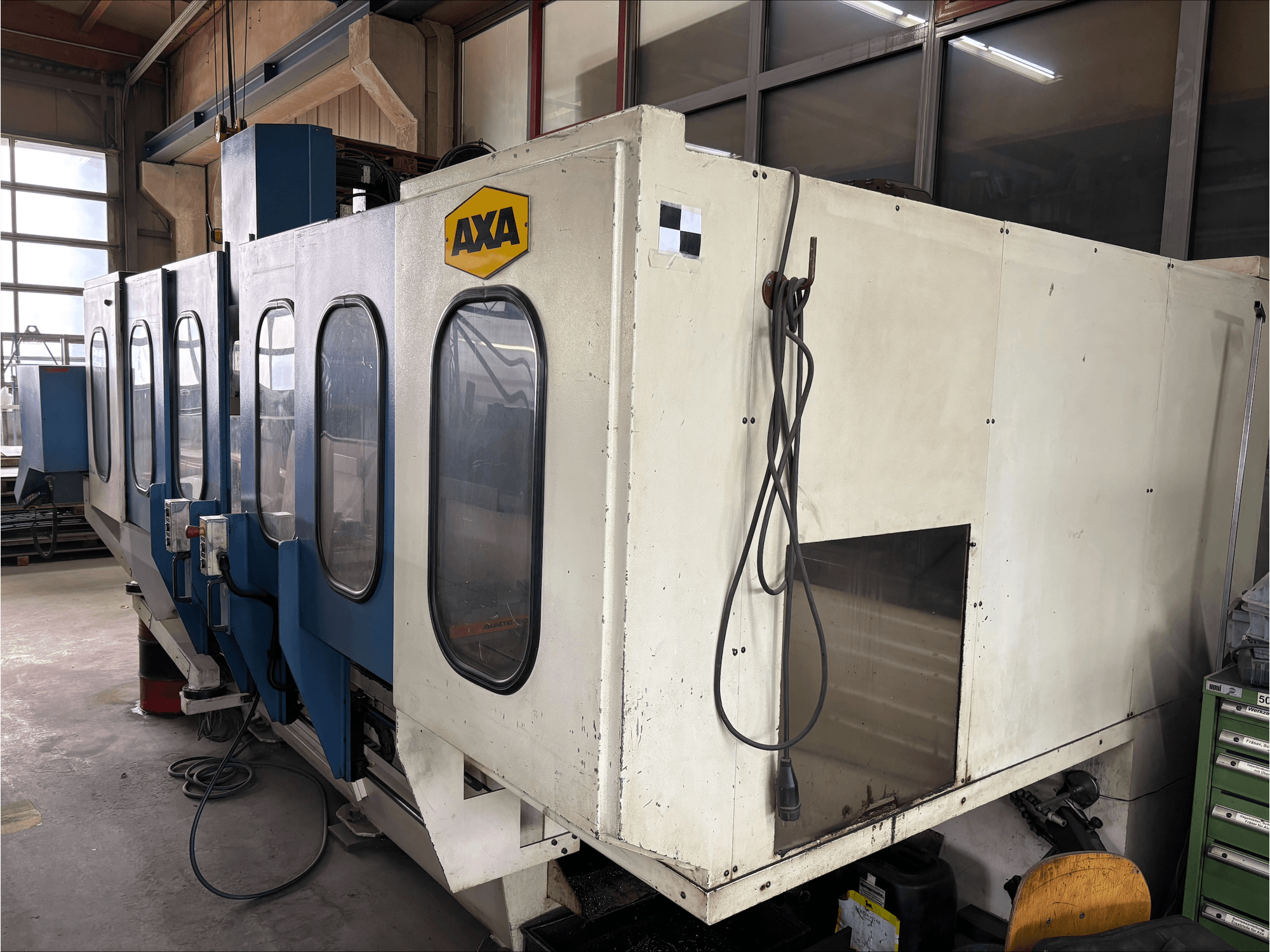 AXA VSC-1-M/C függőleges megmunkálóközpont, elölnézetből, nagy fehér szekrénnyel és kék vezérlőpanellel.